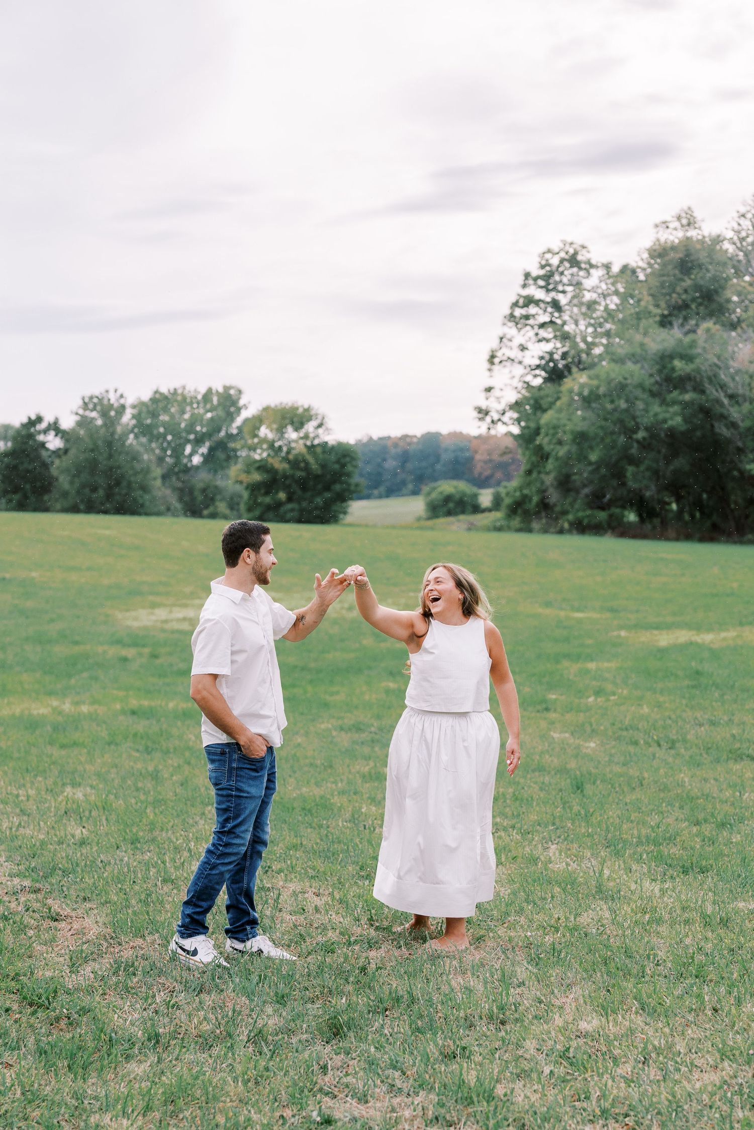 Dancing and twirling in a grassy meadow wearing coordinated white outfits.