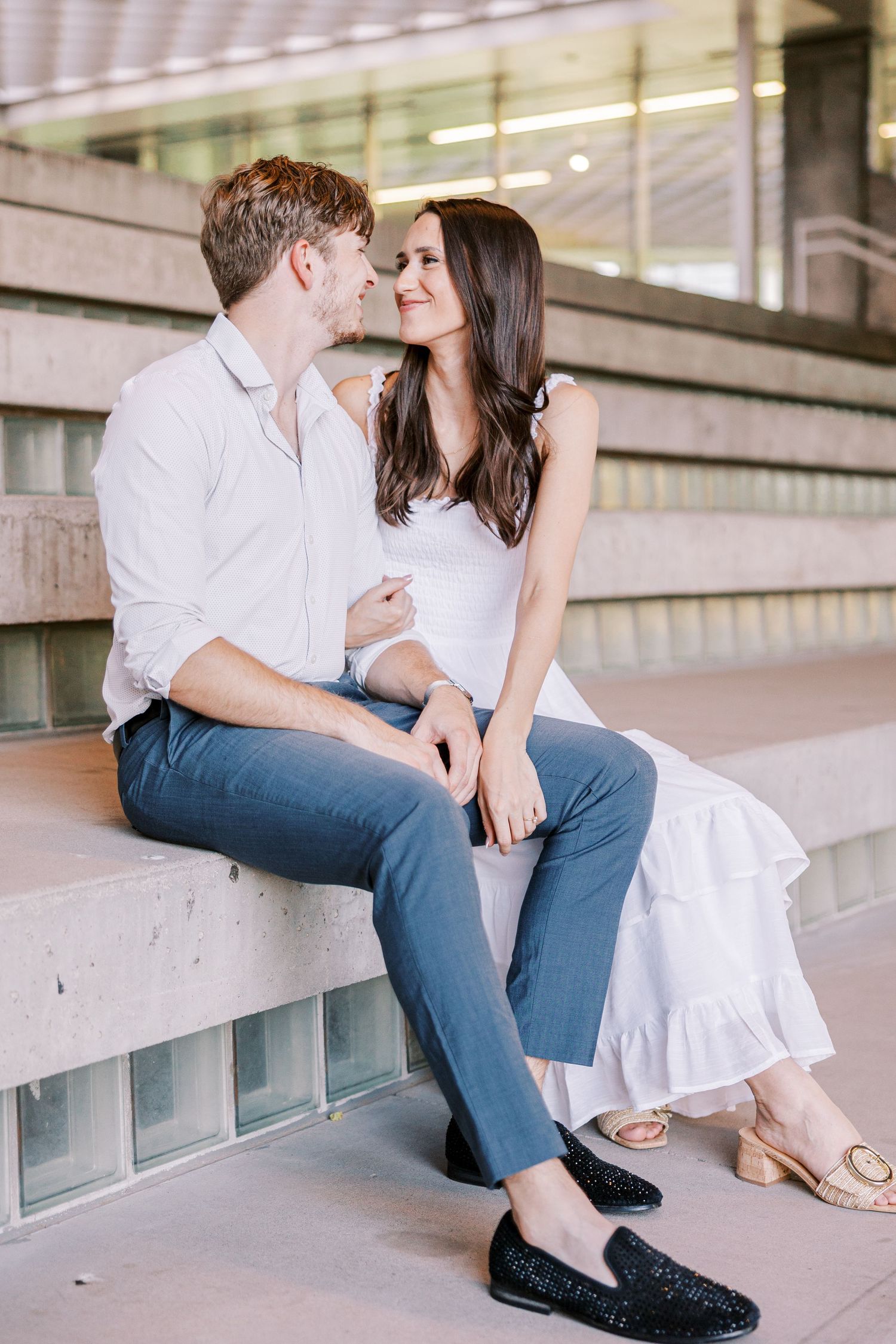 A couple in casual attire sharing an intimate moment while sitting on concrete steps in an urban setting.