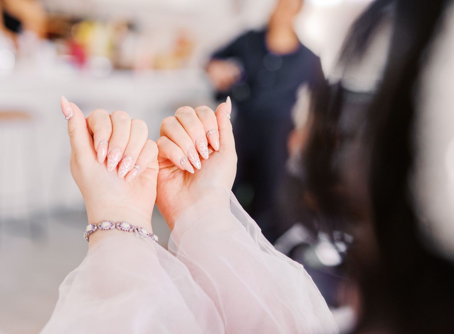 Close-up view of two hands forming a heart shape gesture with delicate bracelet visible against soft blurred background.