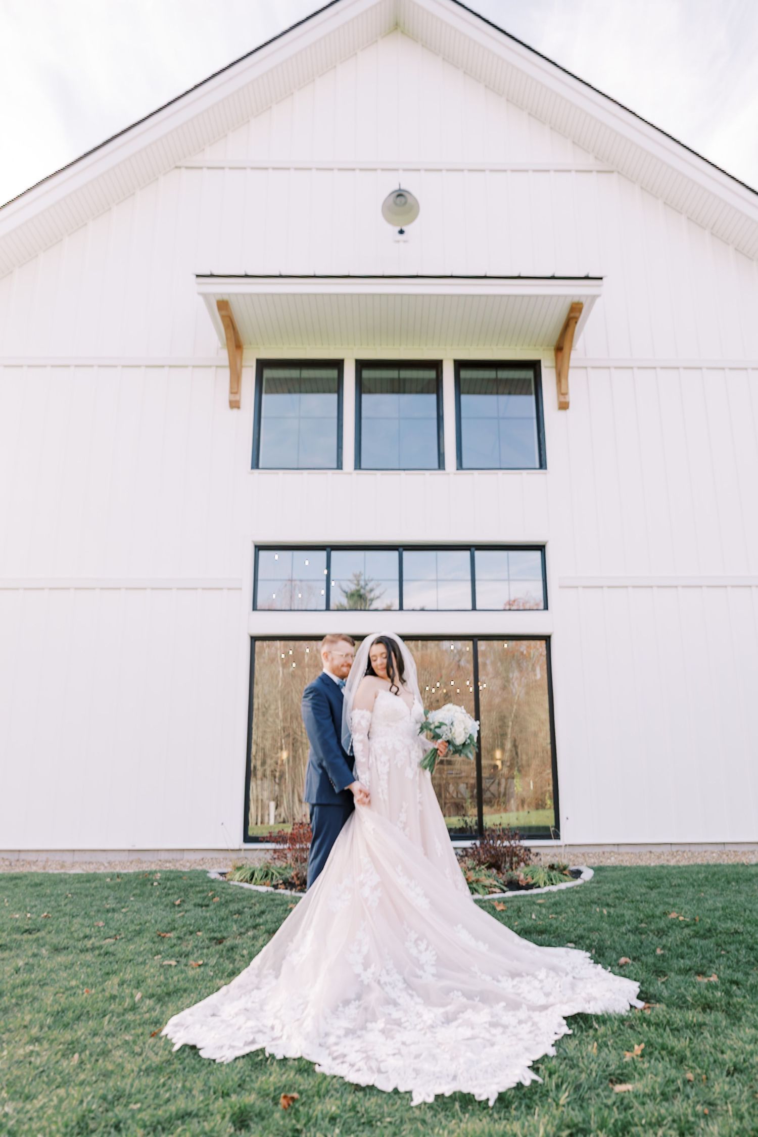 A couple in wedding attire poses in front of a modern white building with large windows.