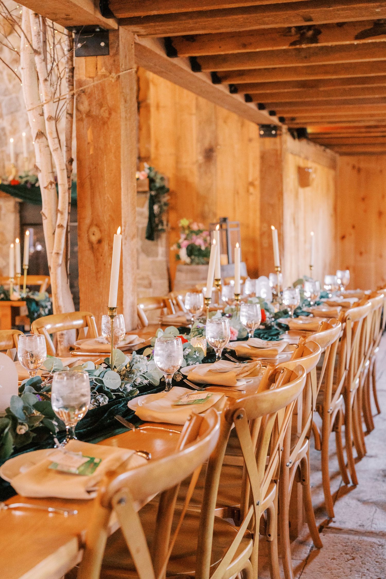Long rustic wooden table set for wedding reception with elegant place settings and greenery garland centerpieces.
