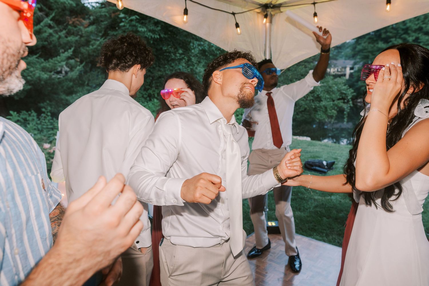 Wedding reception dancing scene with string lights overhead in outdoor setting.