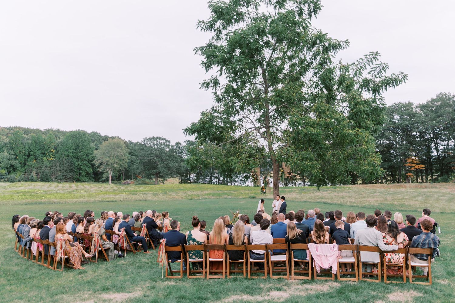 Panoramic view of wedding ceremony site with rows of wooden chairs and guests.