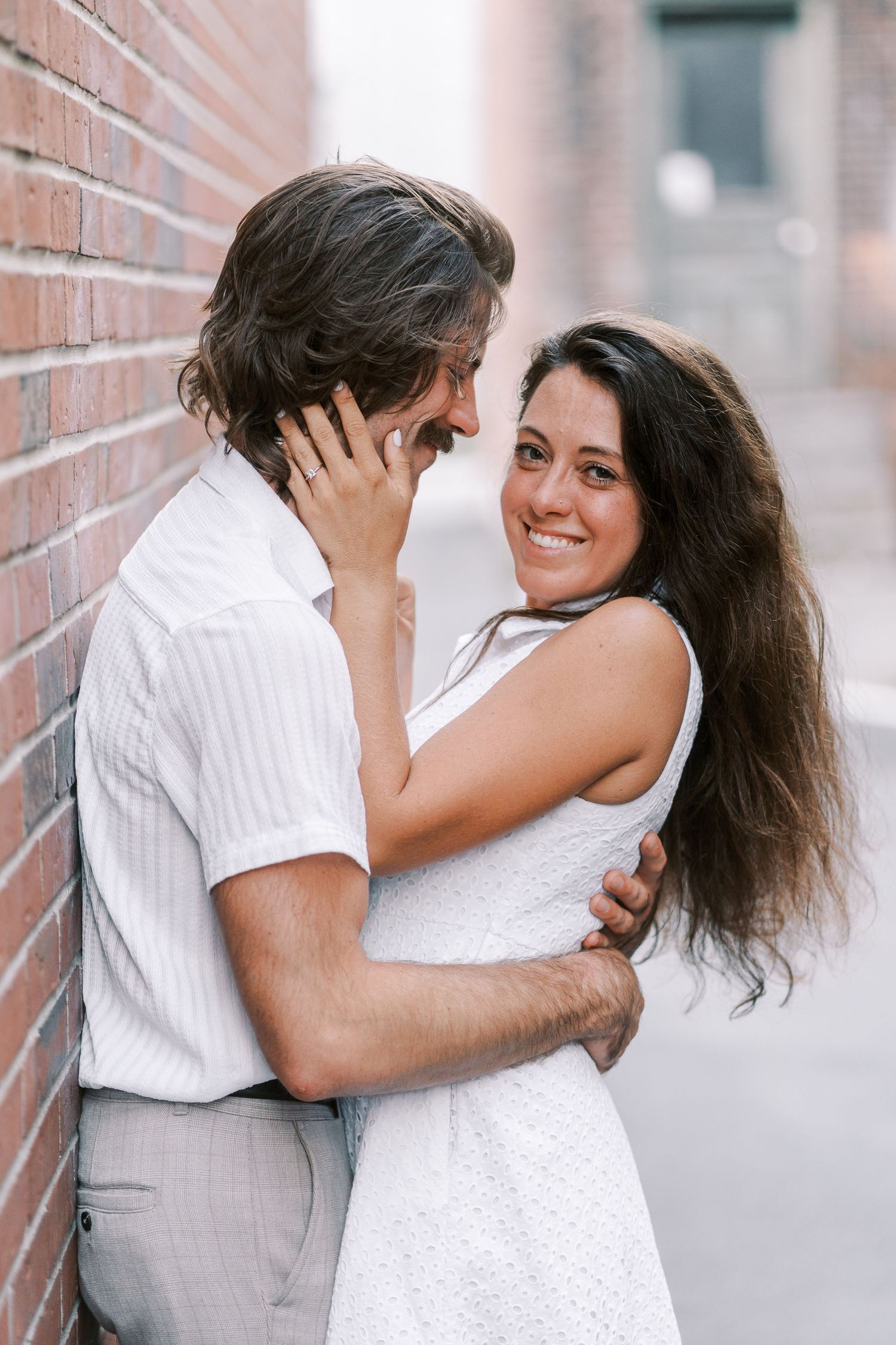 A romantic moment shared against a brick wall background in soft lighting.