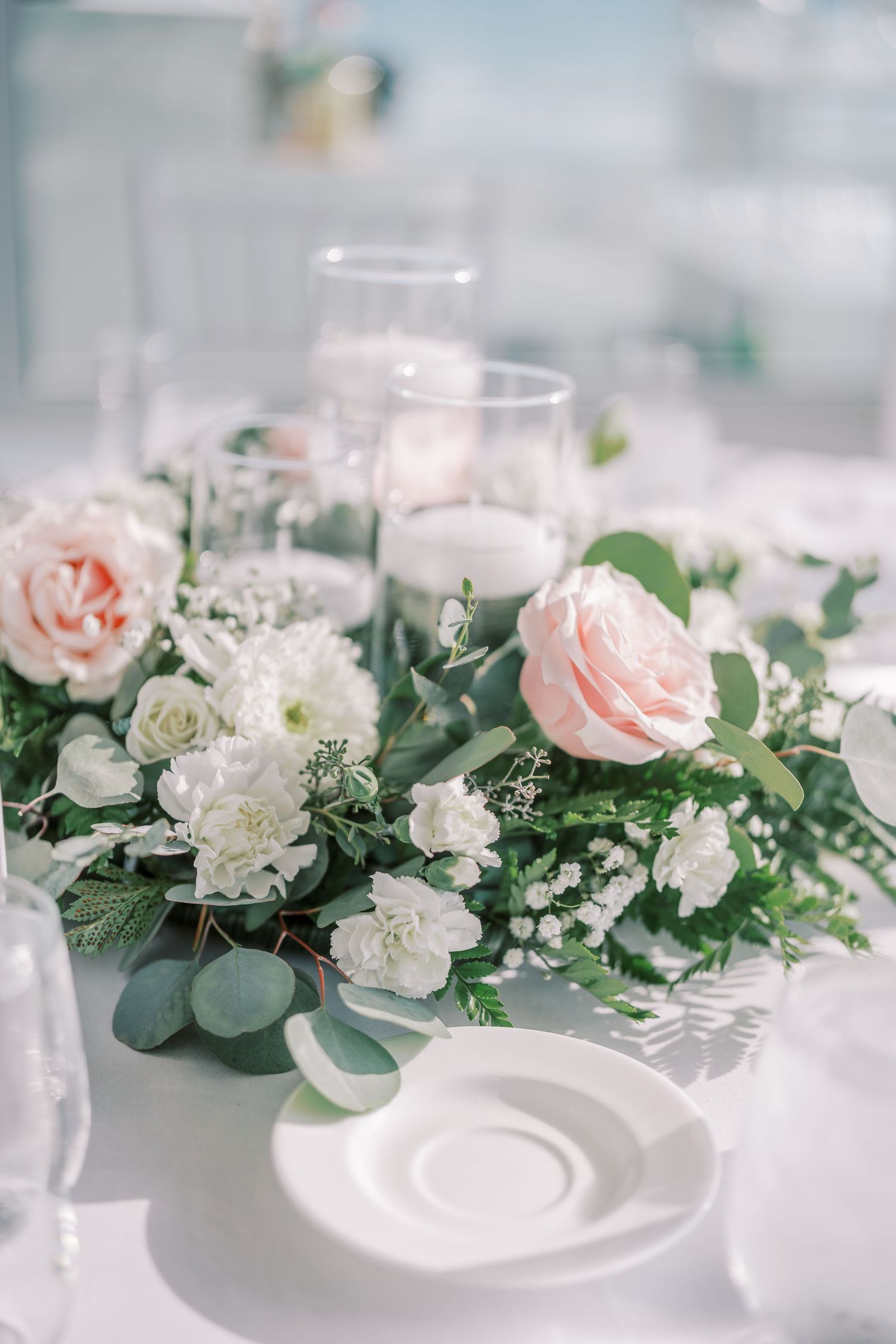 Elegant floral table setting with pink roses, white carnations, and eucalyptus leaves arranged on white plates.