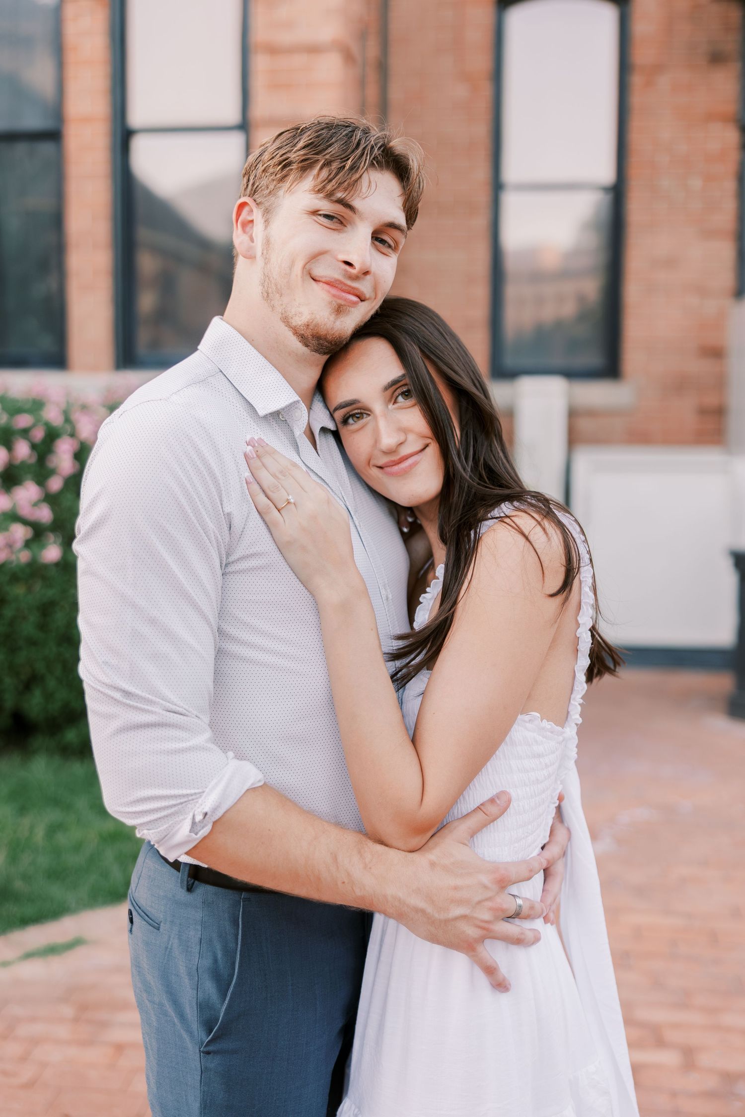 Romantic couple embracing against brick building backdrop with soft natural lighting.