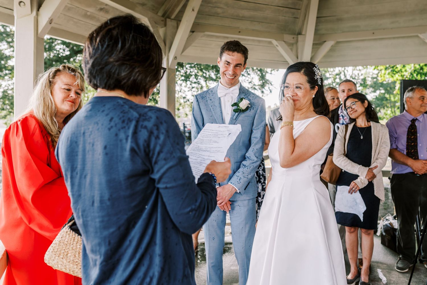 Wedding celebration under a white wooden gazebo with guests gathered around.