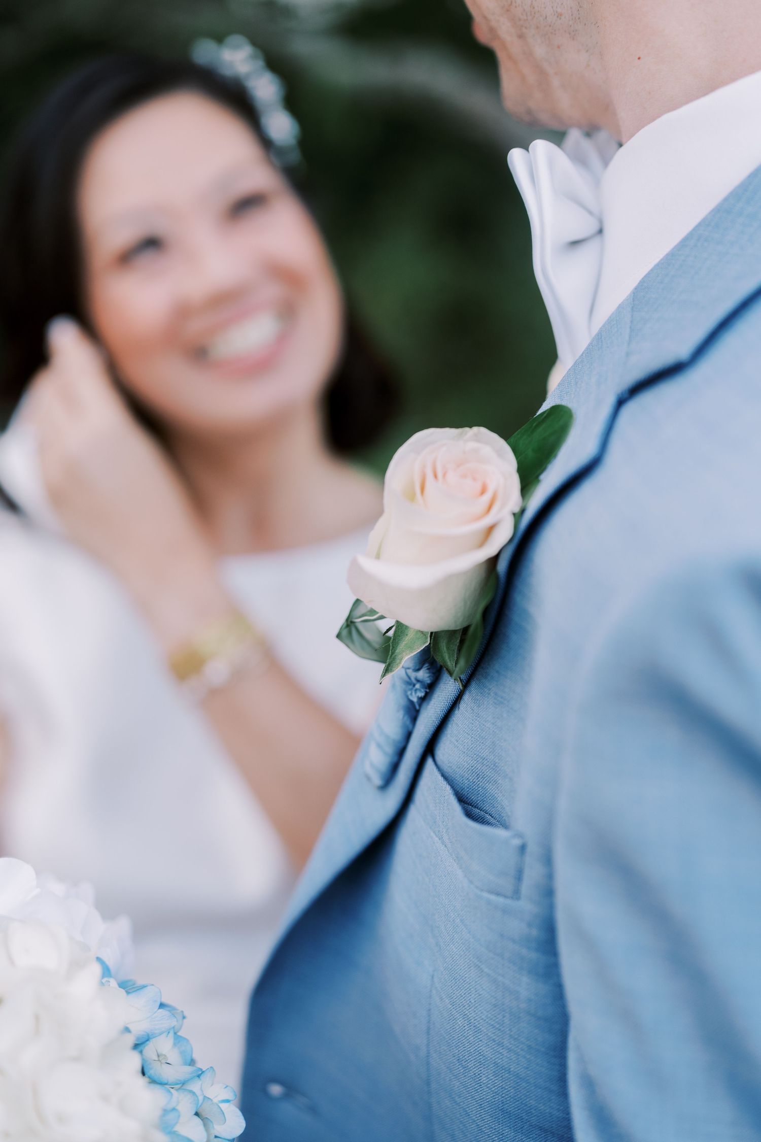 A wedding couple in light blue and white attire share a joyful intimate moment during their outdoor celebration.