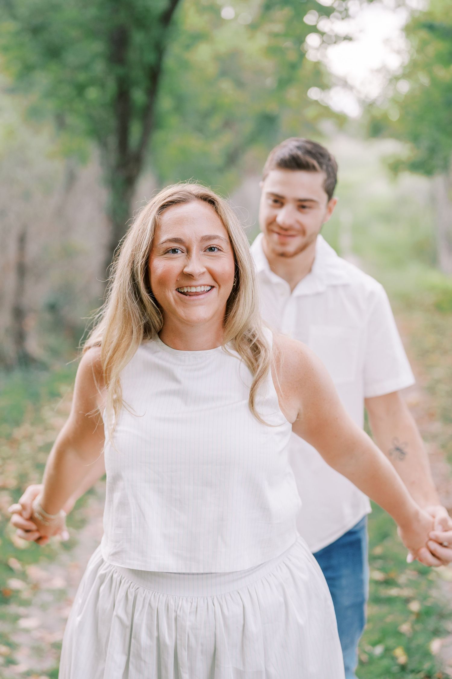 Joyful couple in white outfits having fun during outdoor photo session.