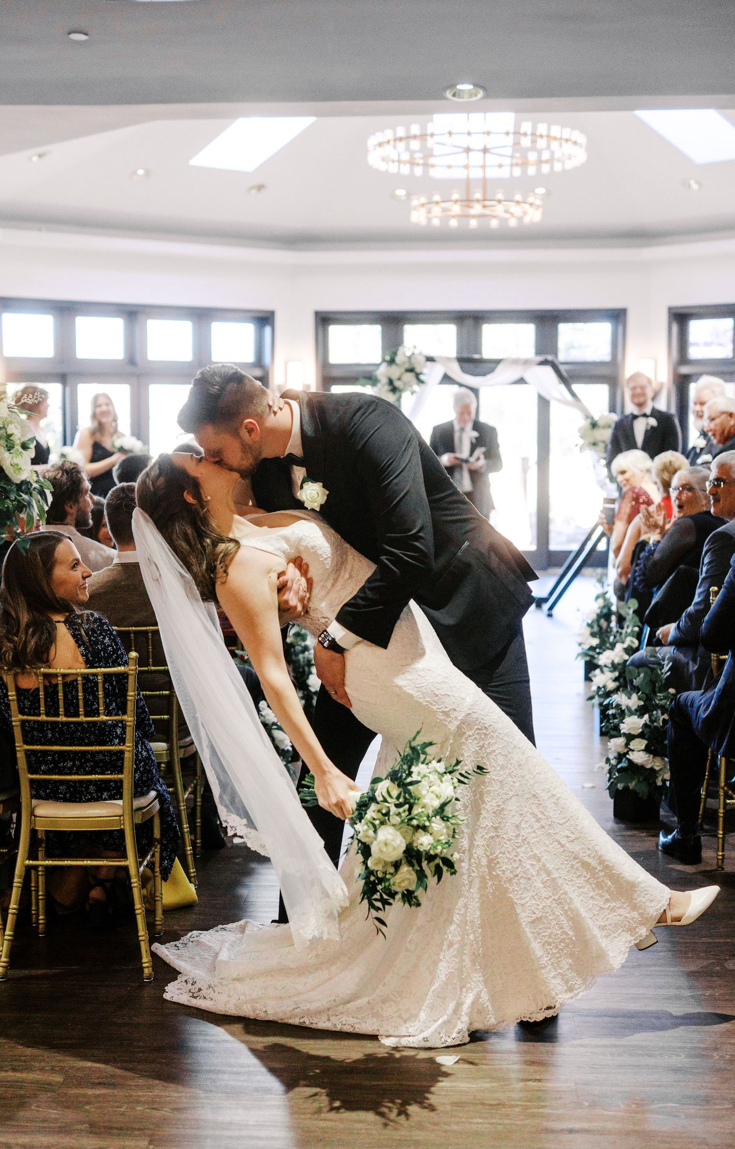 A romantic wedding moment captured as the newlyweds share a dramatic dip kiss in front of seated guests.