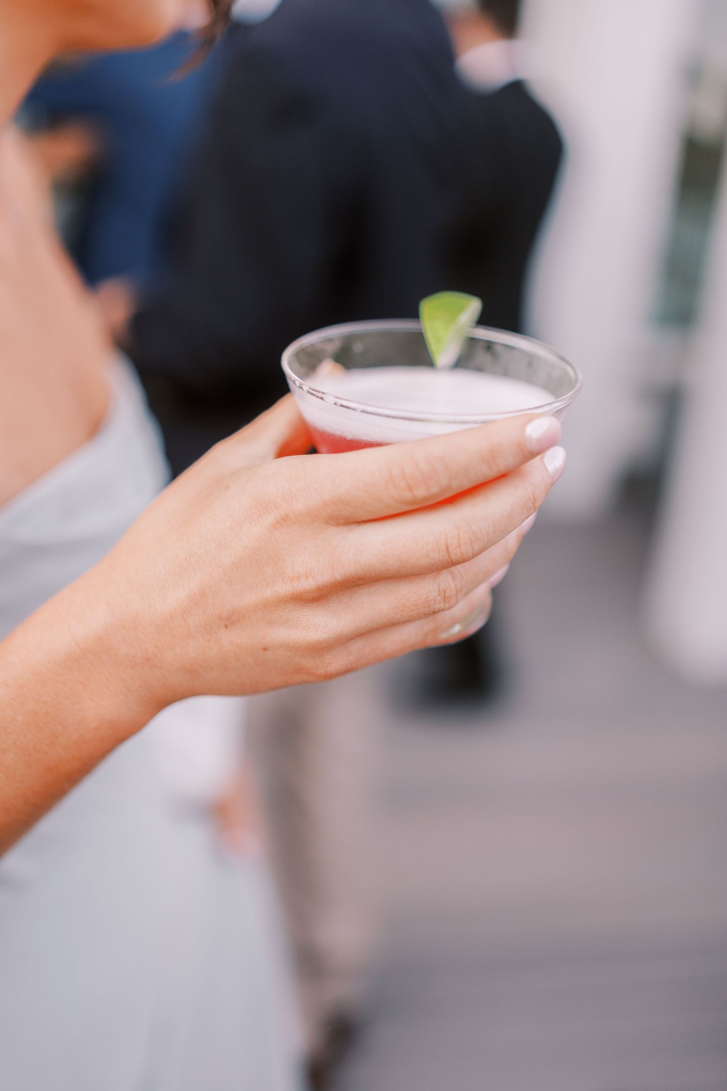 Hand holding a cocktail glass with lime garnish against blurred background.