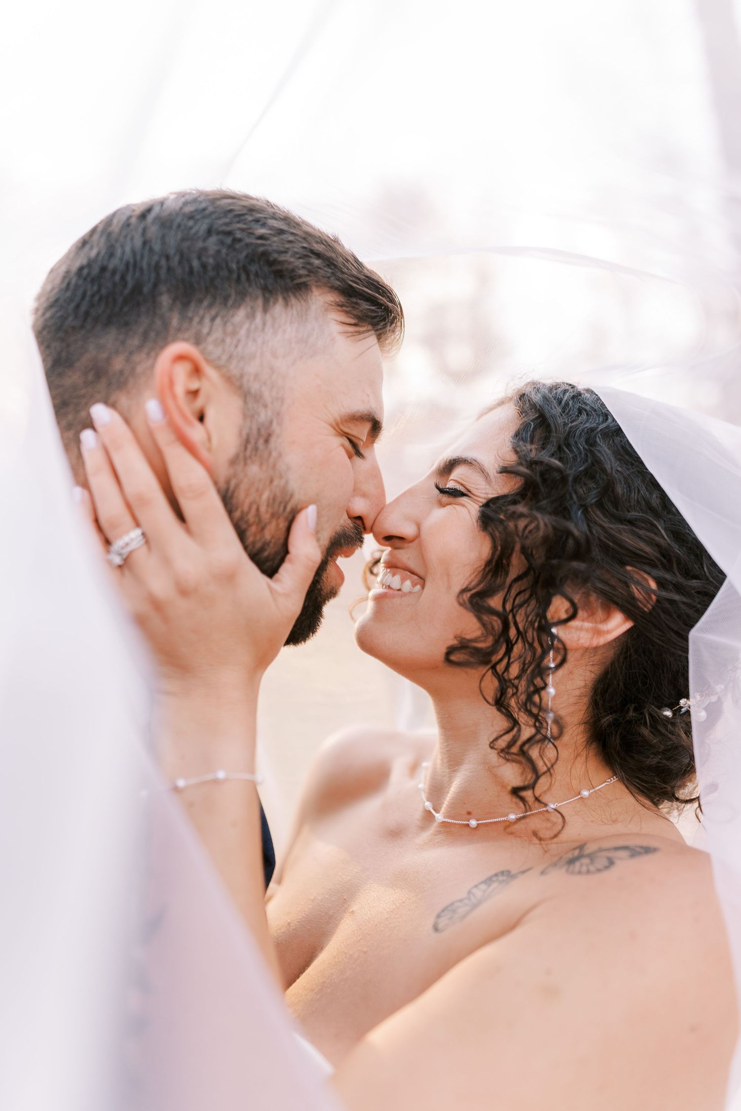 Romantic couple sharing intimate kisses in a dreamy white setting with soft lighting and tender expressions.