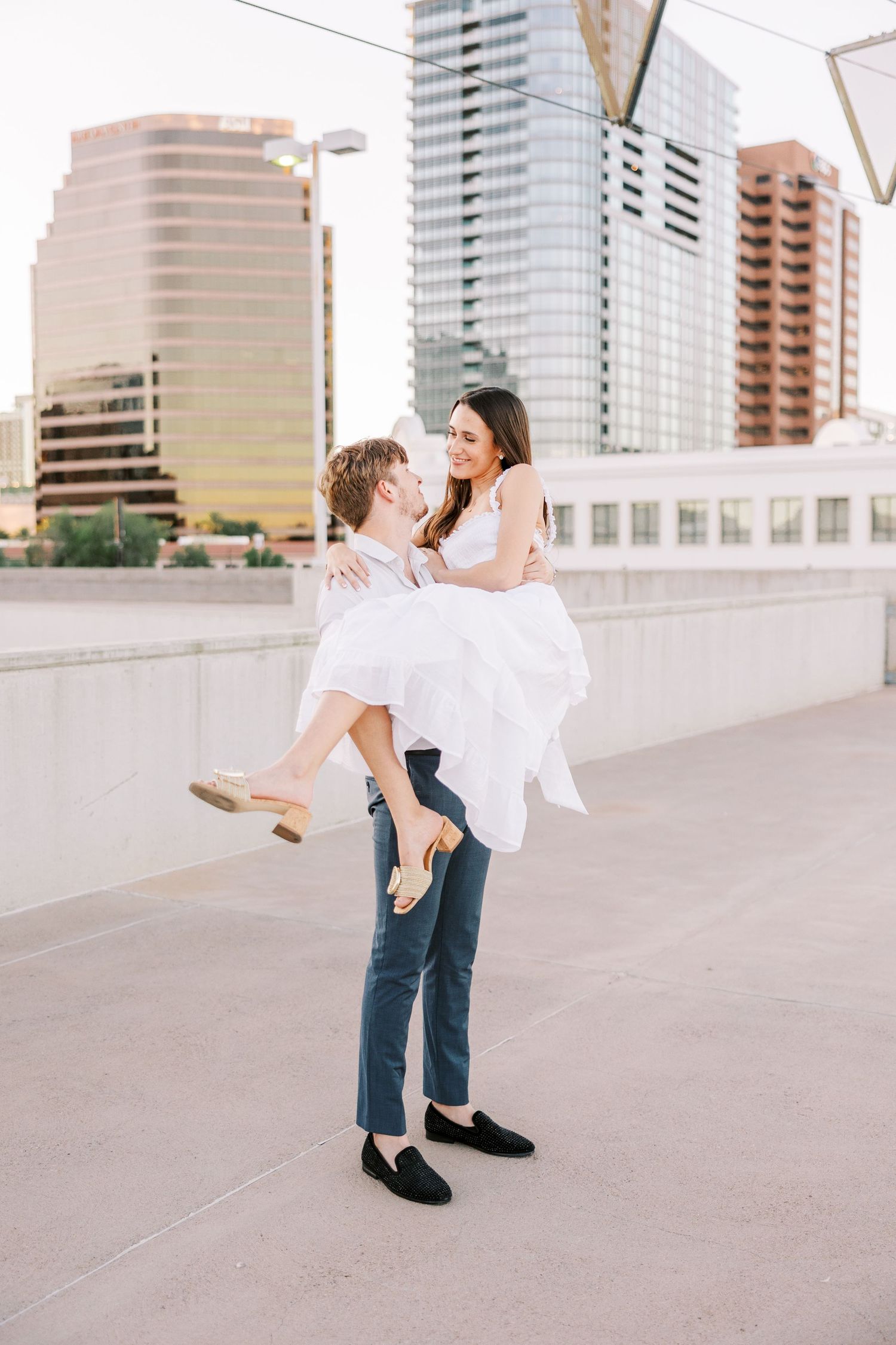 A playful couple dancing together on an urban rooftop with city buildings in the background.