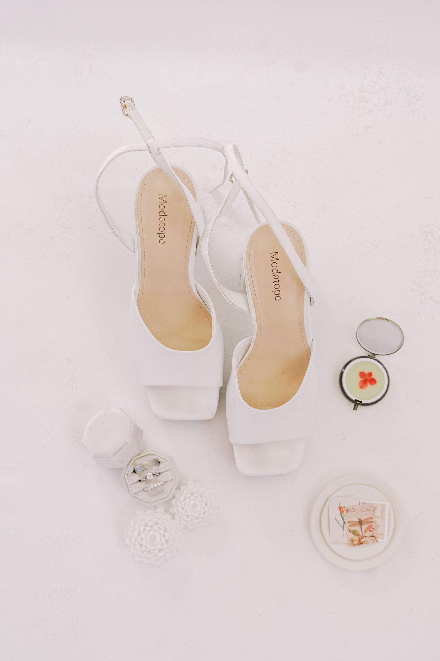 White bridal shoes and delicate lace accessories arranged on a light background in a minimalist wedding styling composition.