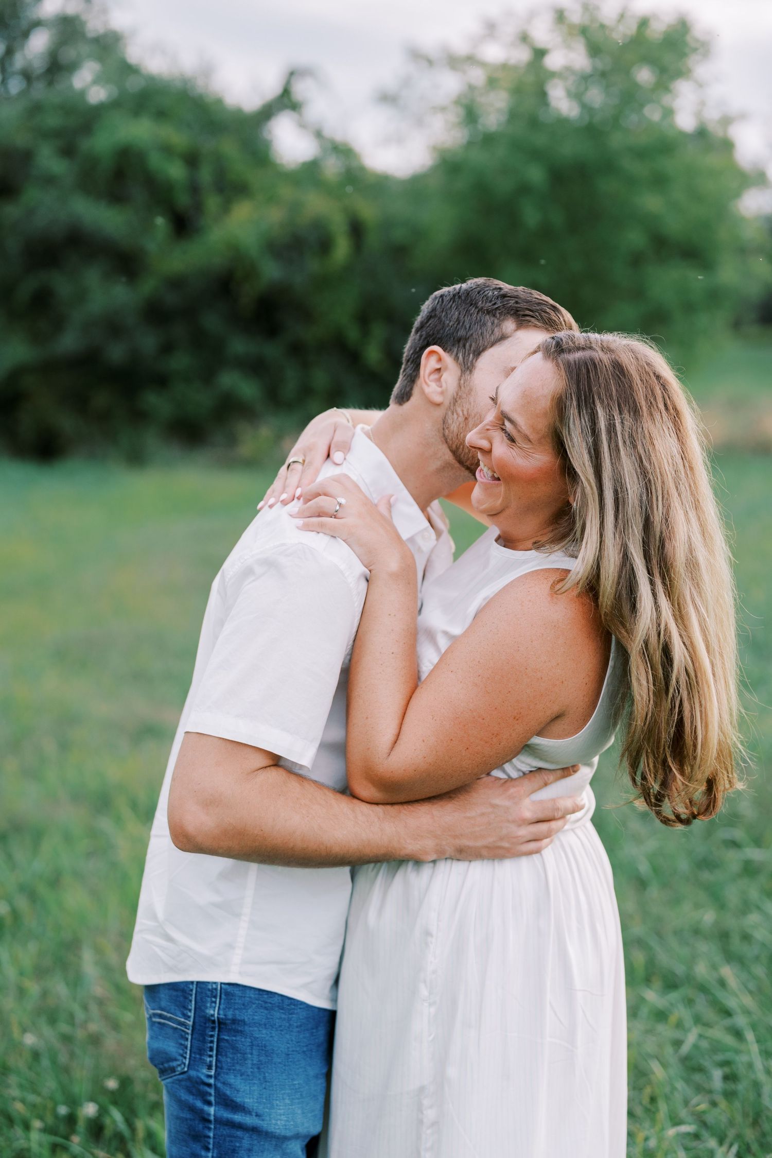 A romantic couple in white clothing sharing tender moments in a green summer field.