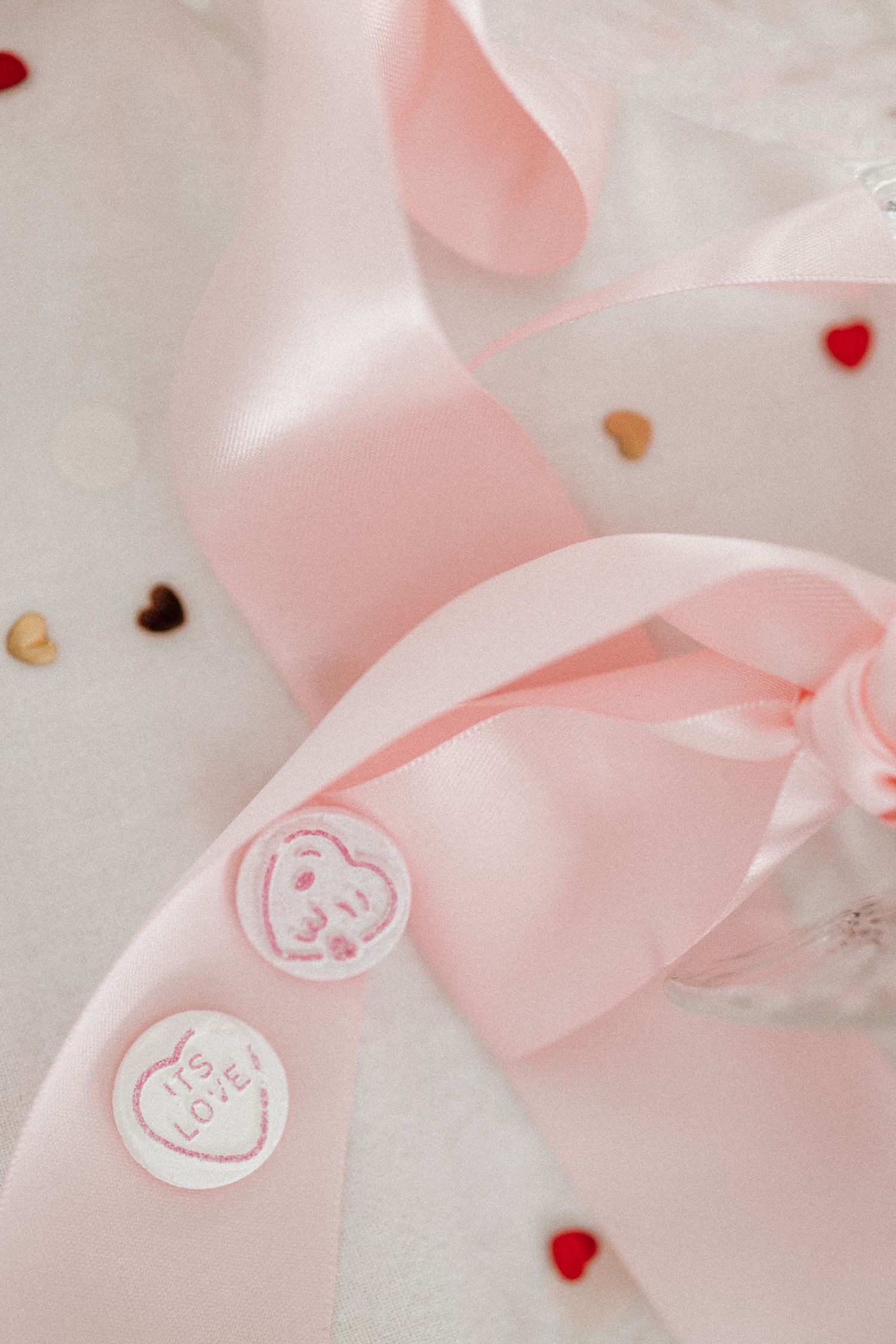 Pink satin ribbon with love heart wax seal stickers and confetti on white background.