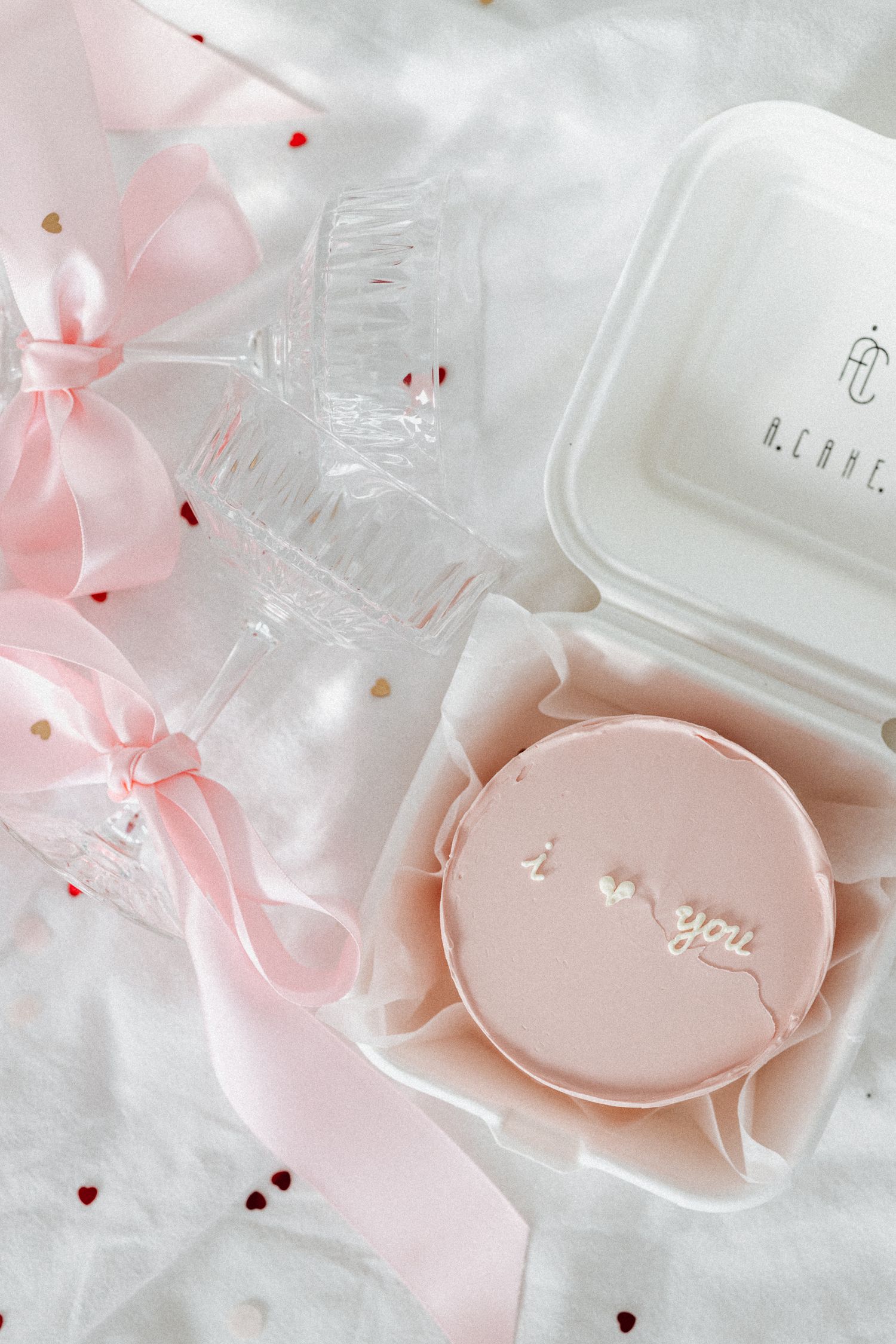 Pink bento cake with i love you decoration in white box with ribbon and champagne flute for Valentine's Day.