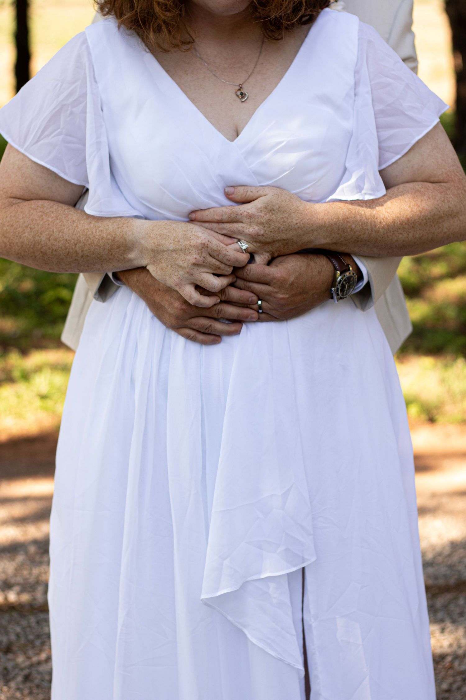 Woman wearing a flowing white summer dress stands in dappled sunlight outdoors.