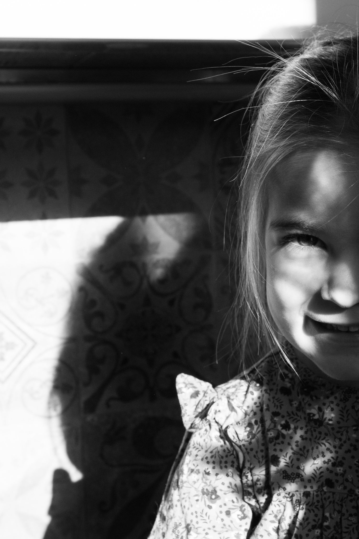 A black and white portrait with dramatic lighting and shadows casting across a floral dress pattern.