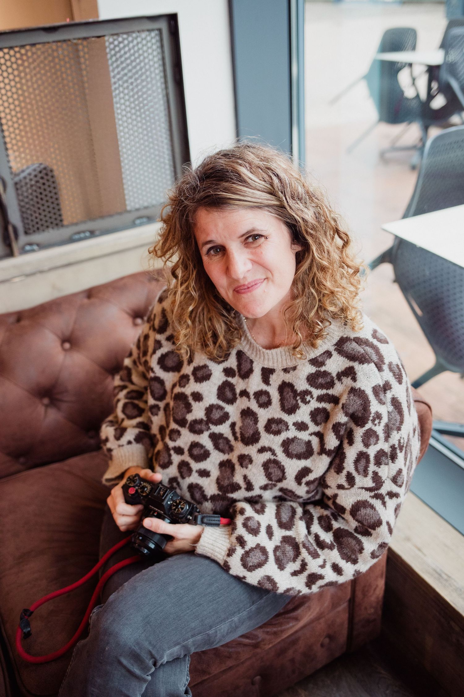 Woman in leopard print sweater relaxes on brown leather couch near window.
