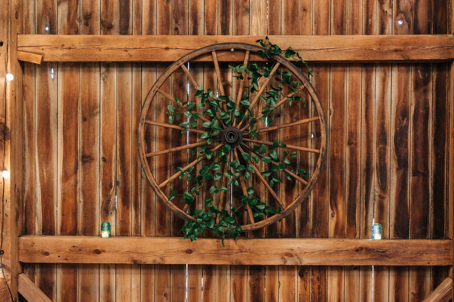 Decorative wooden wagon wheel adorned with greenery mounted on rustic barn wall.