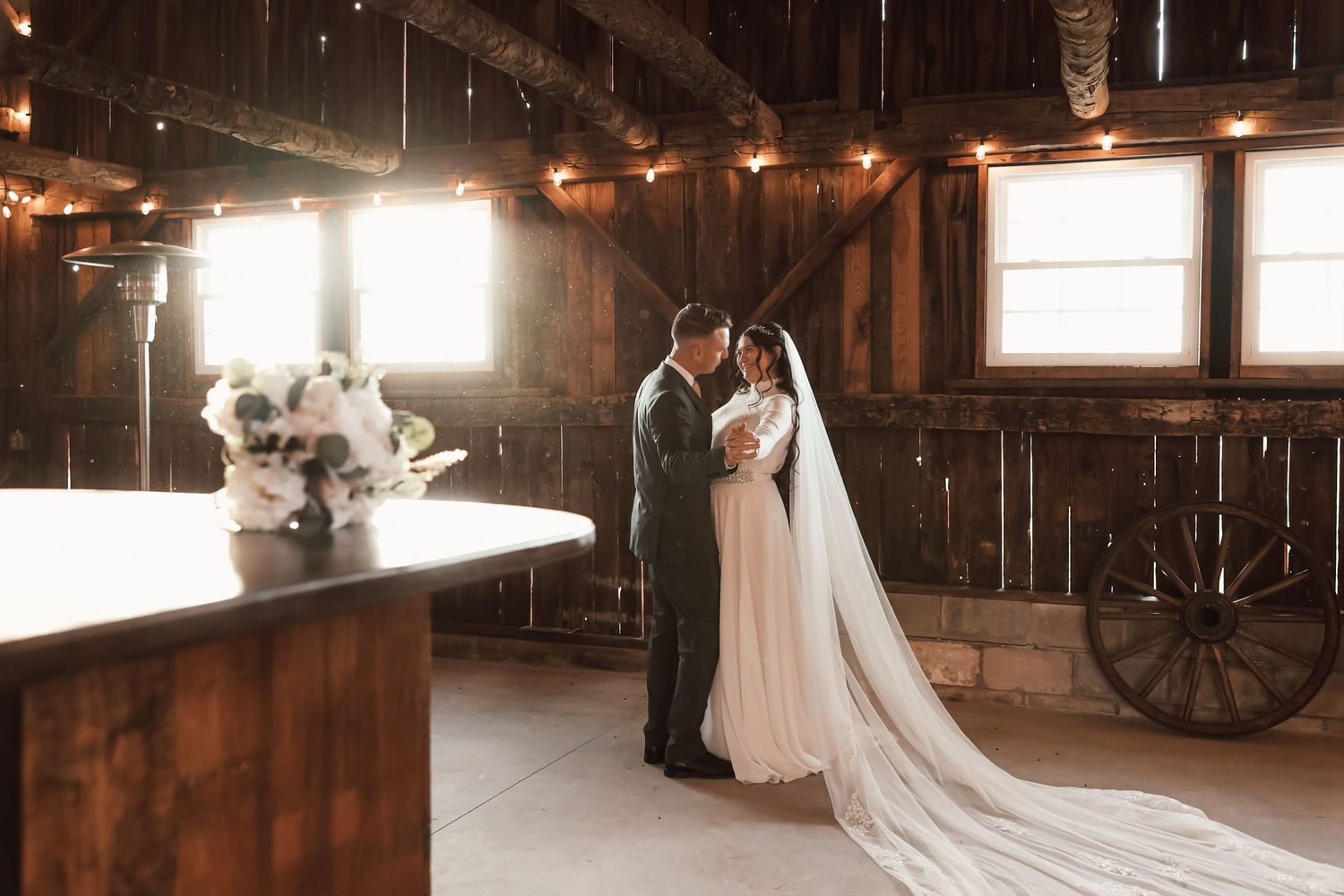 A romantic couple poses together in a rustic wooden barn with sunlight streaming through the wooden slats.