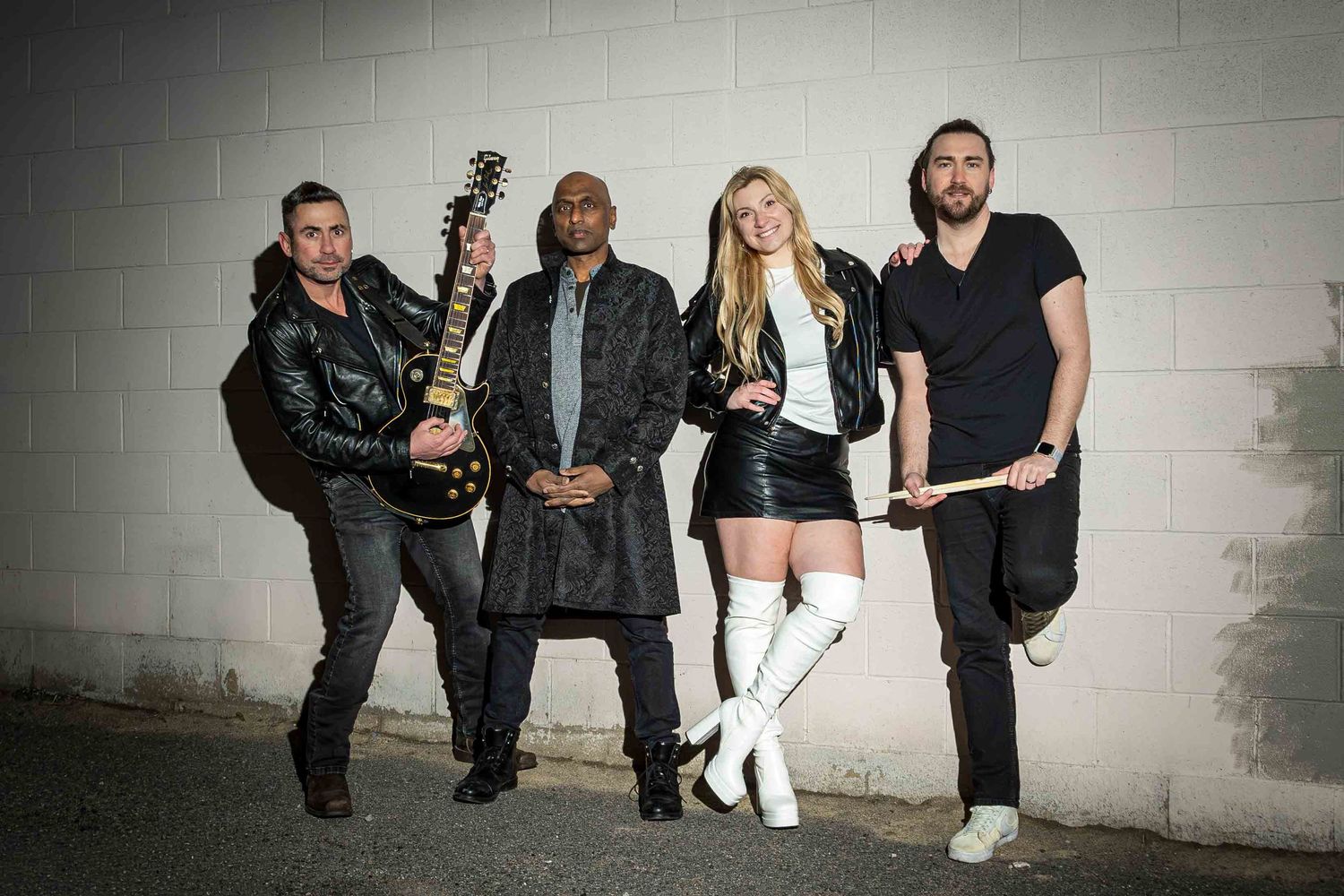 Group of musicians posing against white brick wall in casual attire.