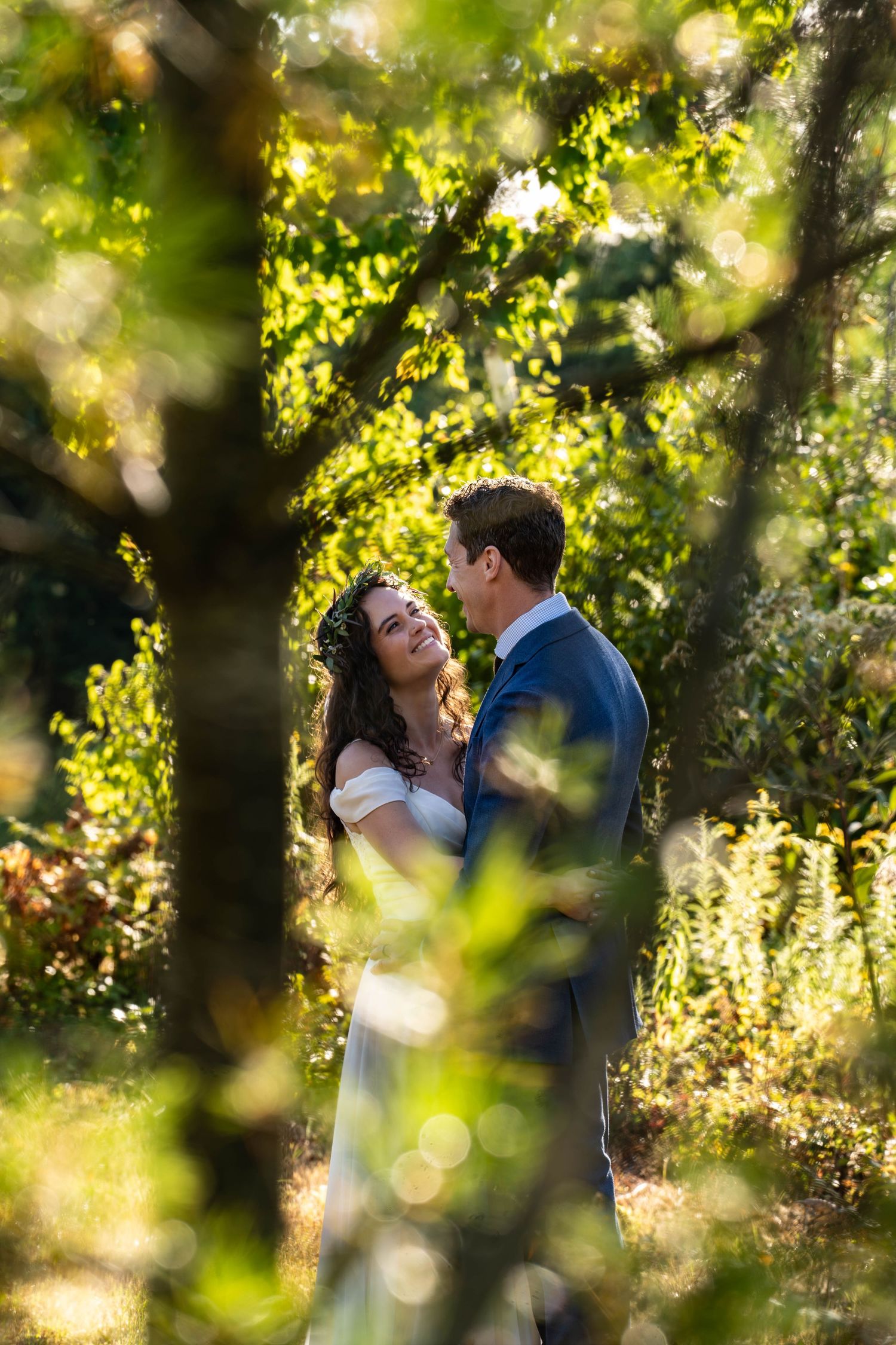 Romantic wedding couple embracing in a sun-dappled forest setting with golden bokeh effects.
