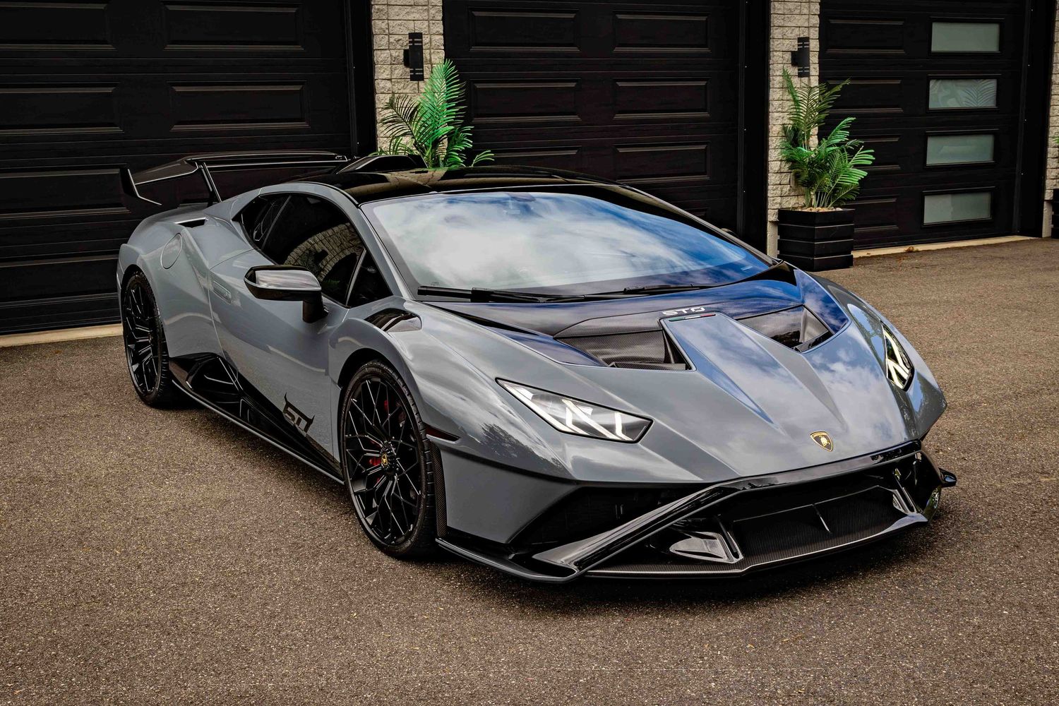 Gray Lamborghini Huracan STO supercar parked on a driveway in front of a modern garage.