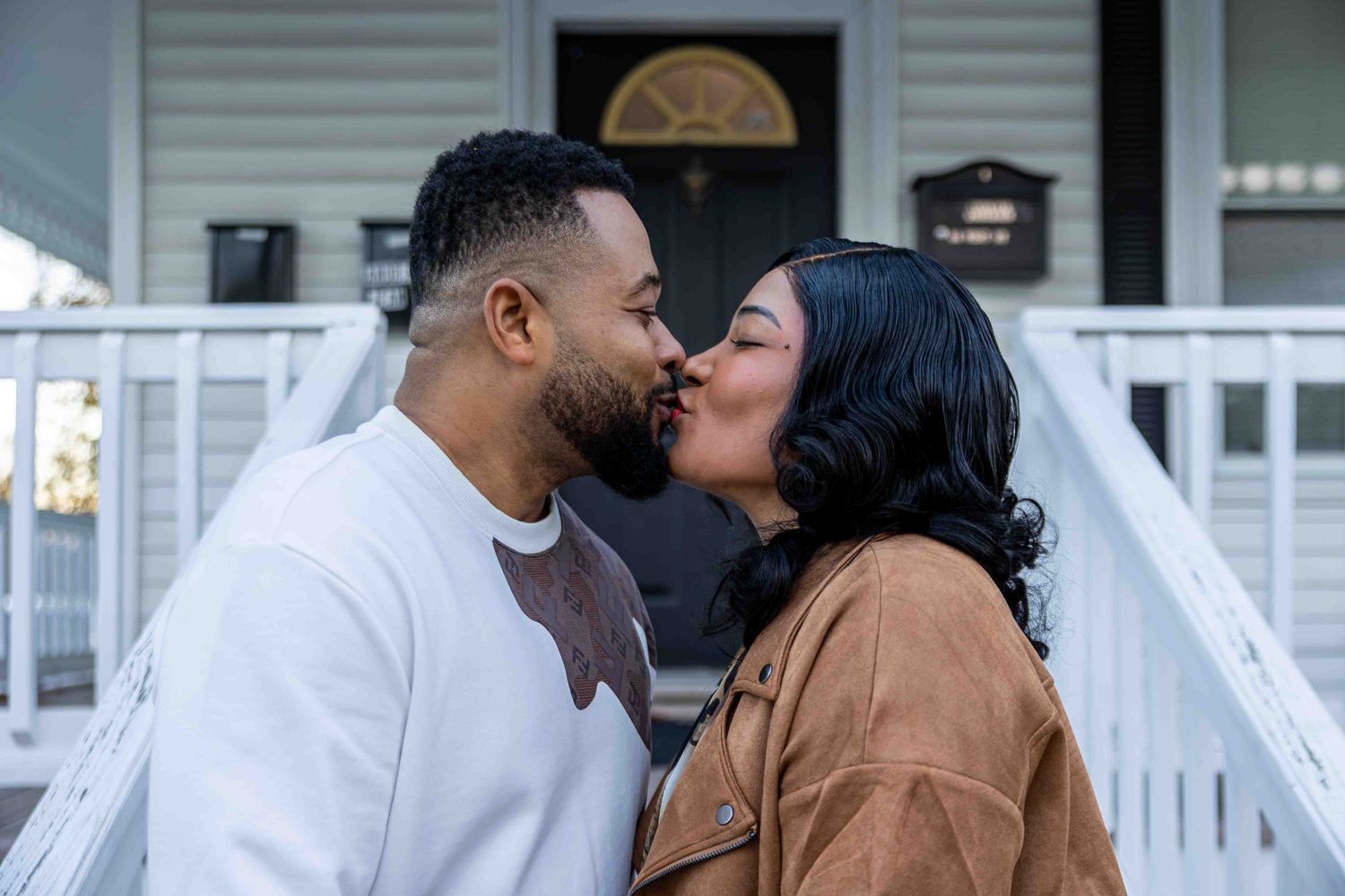 Couple sharing an intimate moment in front of white house porch.