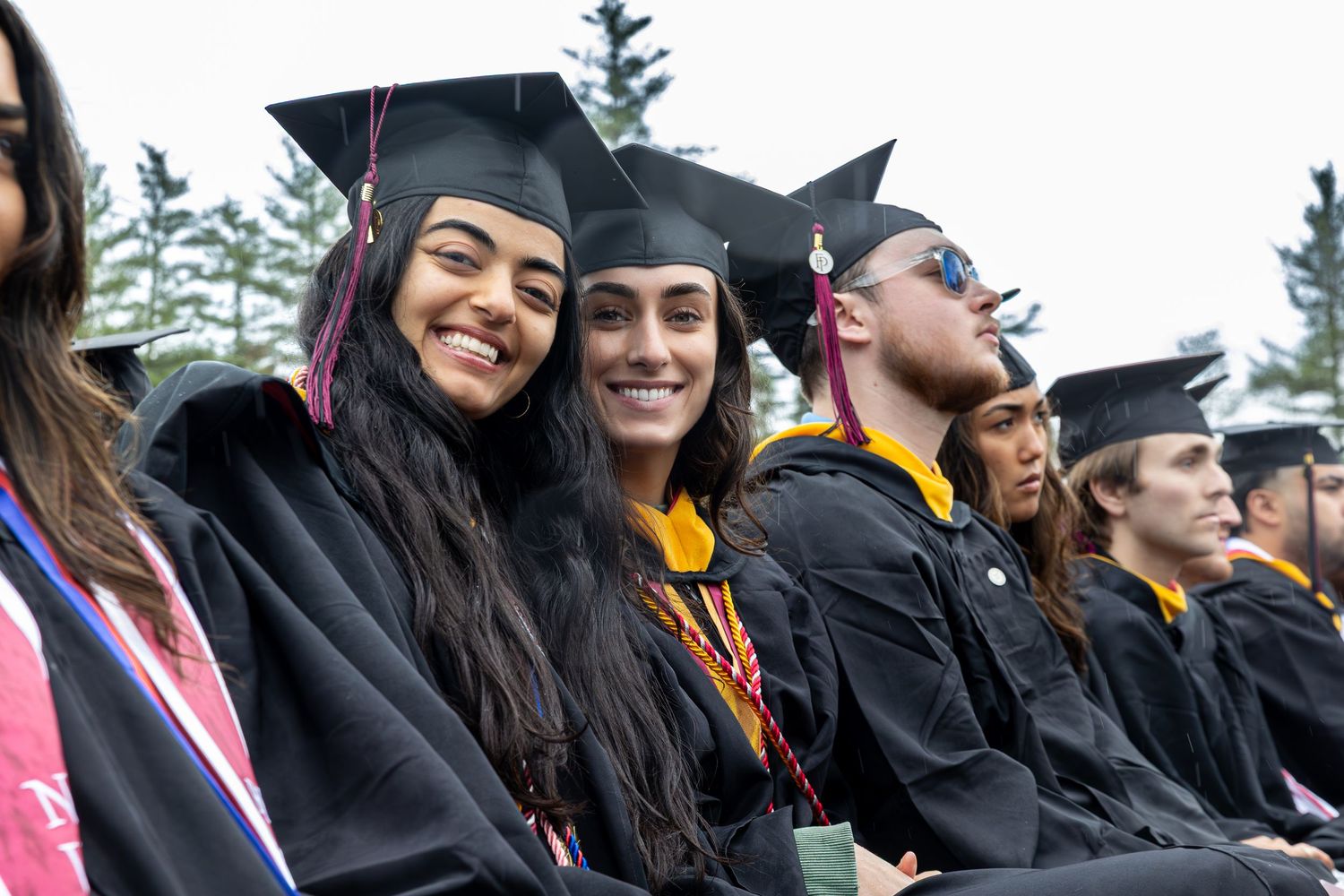 Graduates in black caps and gowns celebrating at an outdoor commencement ceremony.