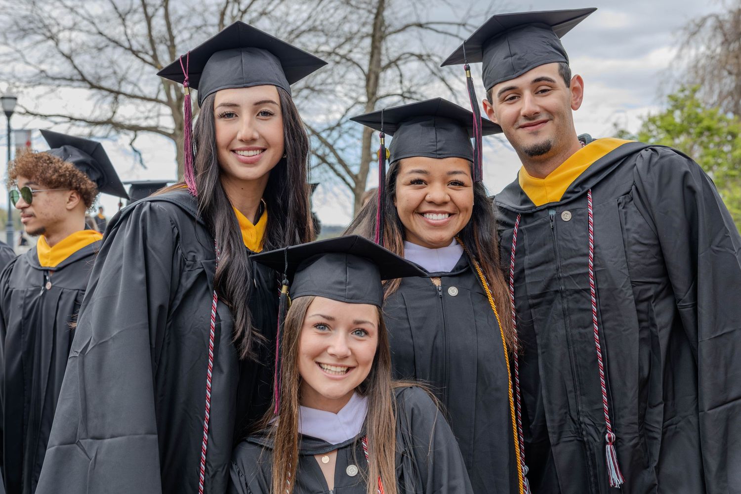Graduates in black caps and gowns celebrate together outdoors on graduation day.