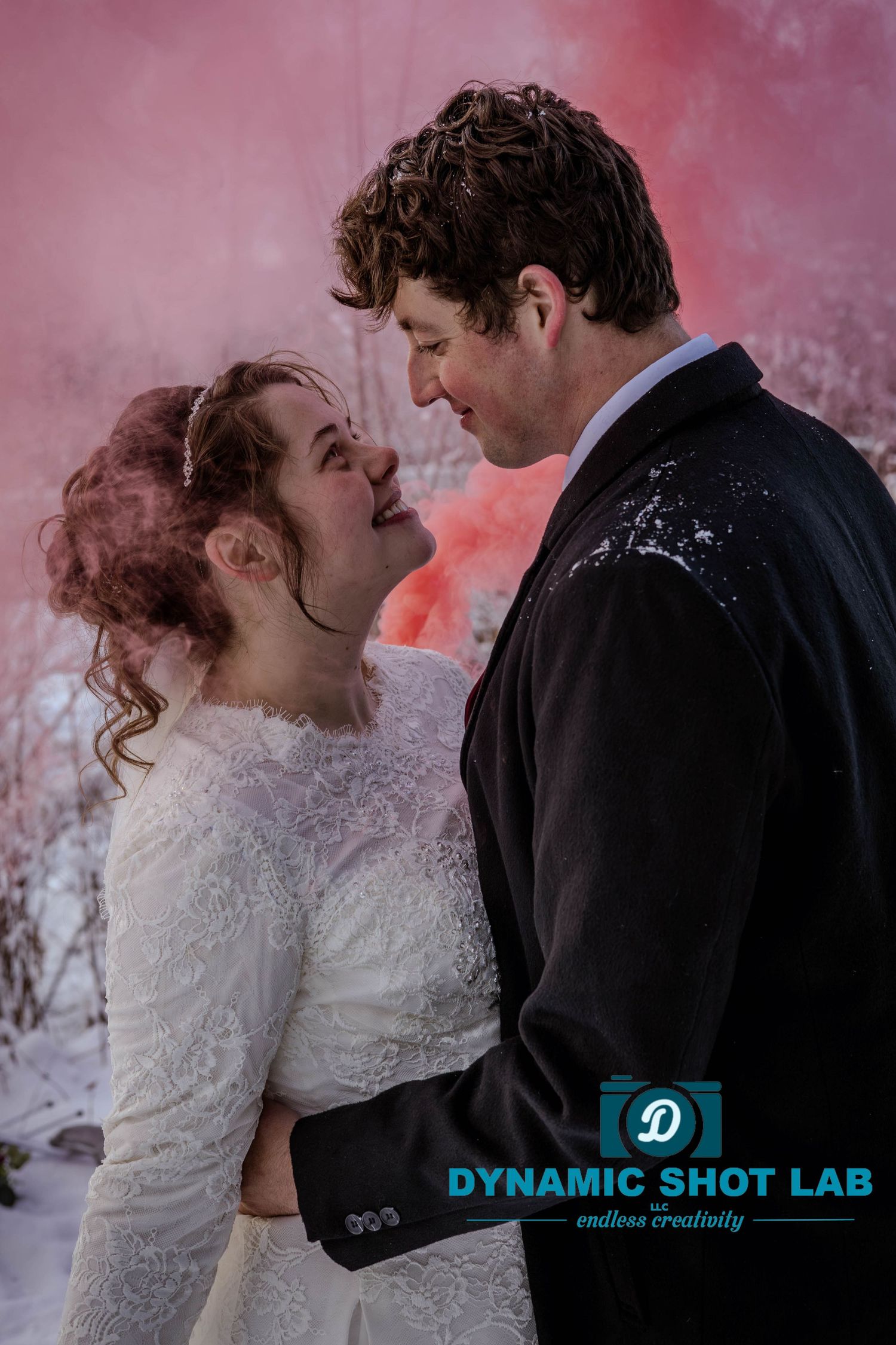 Romantic wedding couple embraces in a dreamy pink-lit setting with a professional photography watermark.