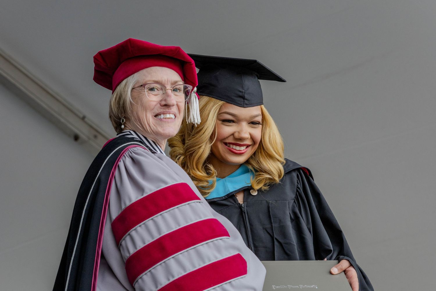 Graduates in red and black academic regalia pose for photos during commencement.