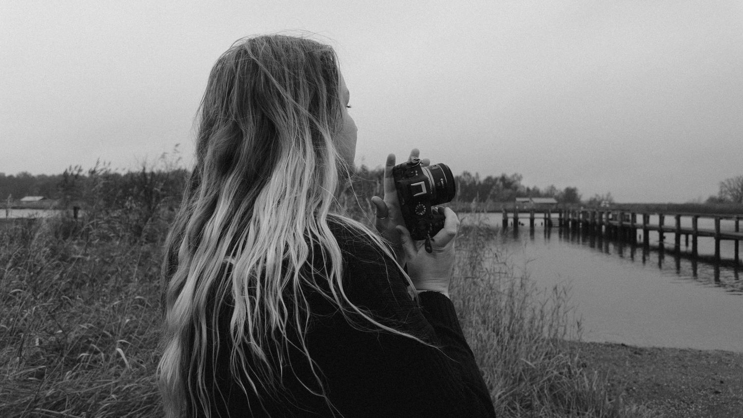 Back view of photographer with flowing hair taking pictures by waterfront.