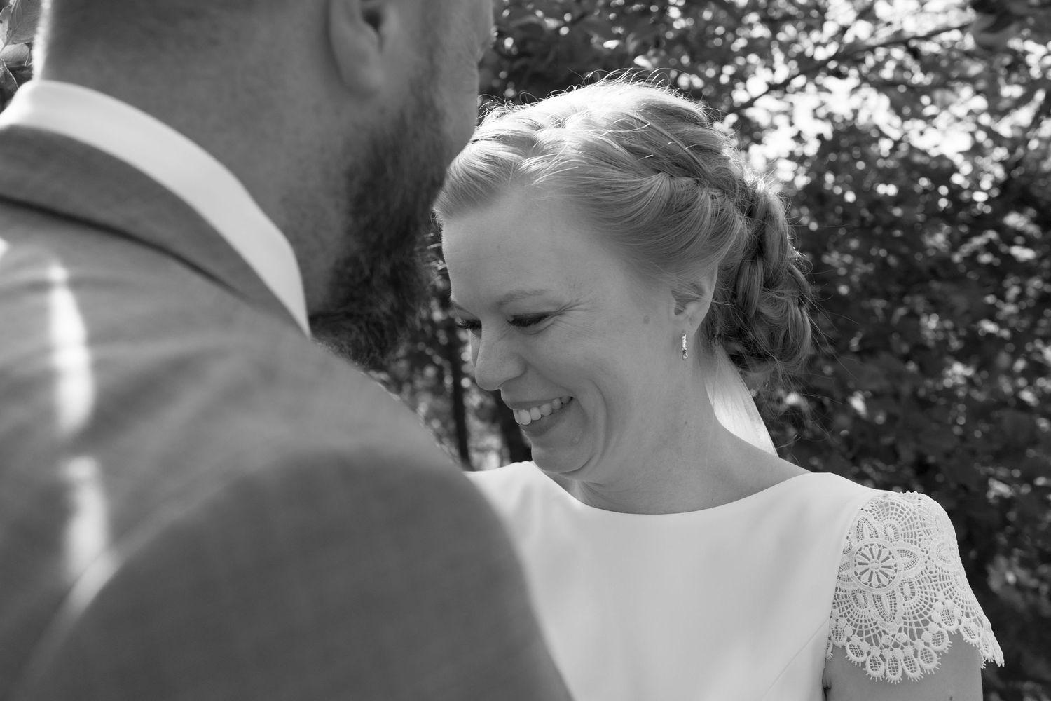 Black and white photo of a joyful moment during an outdoor wedding with couple in formal attire.