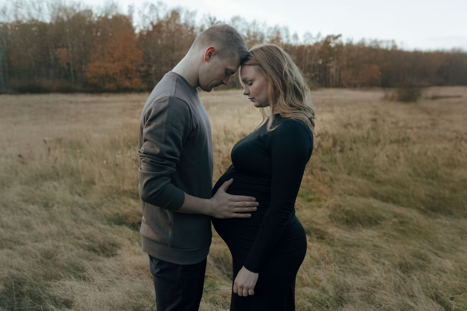 Intimate maternity photo of couple embracing in rustic field during golden hour.