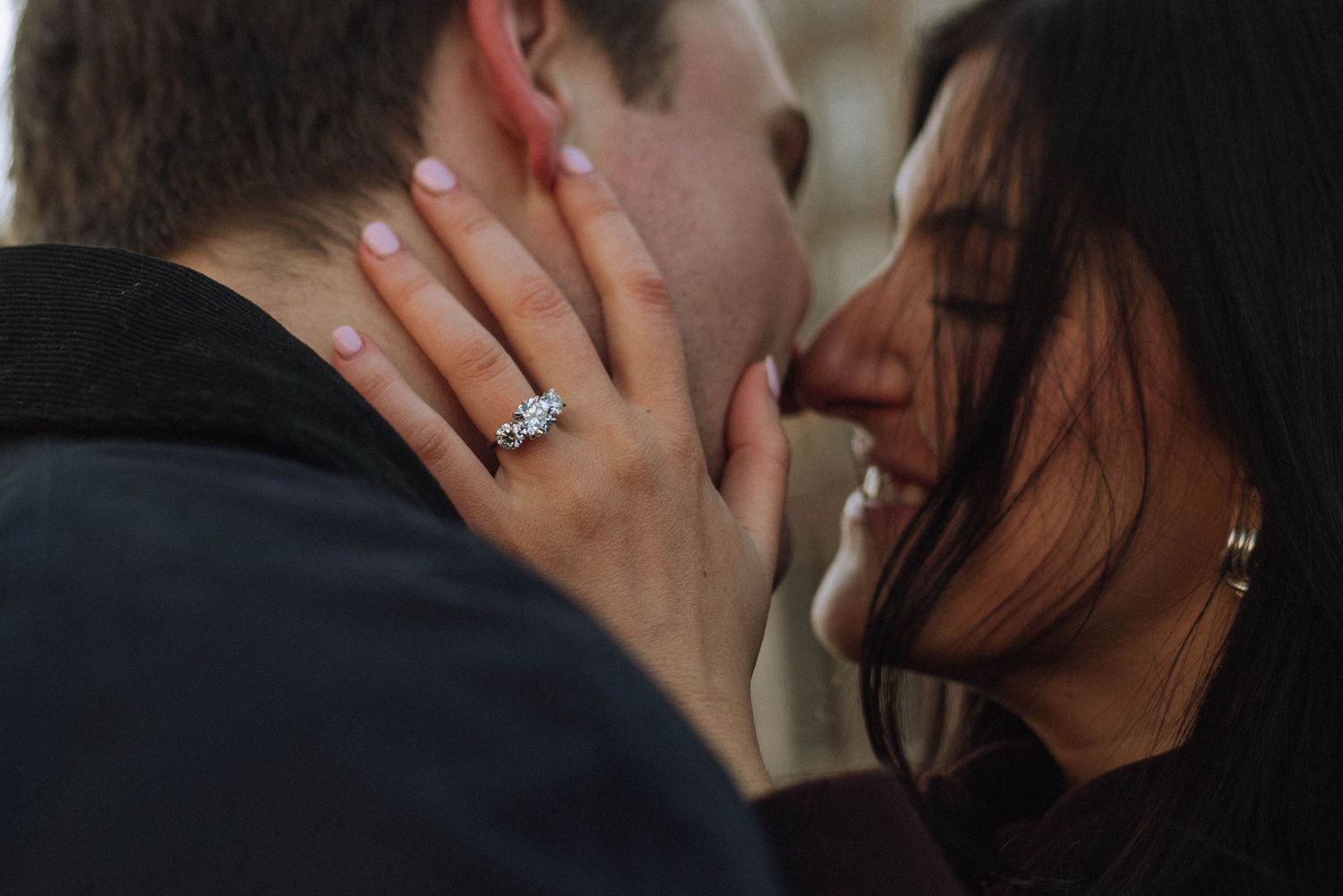 Couple sharing a romantic kiss, woman displaying a stunning diamond engagement ring on her hand.