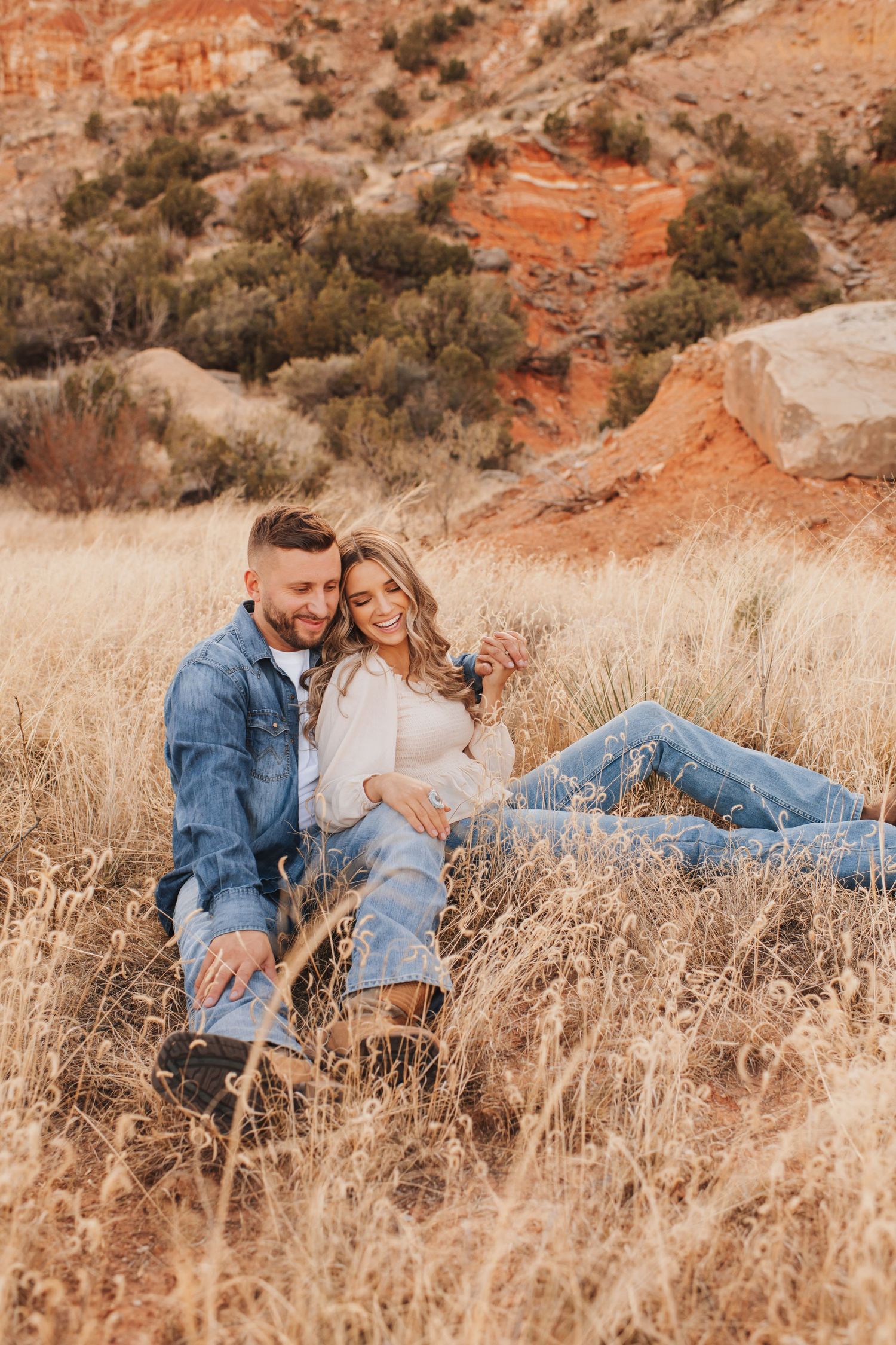 Engaged couple sitting down and smiling in a field