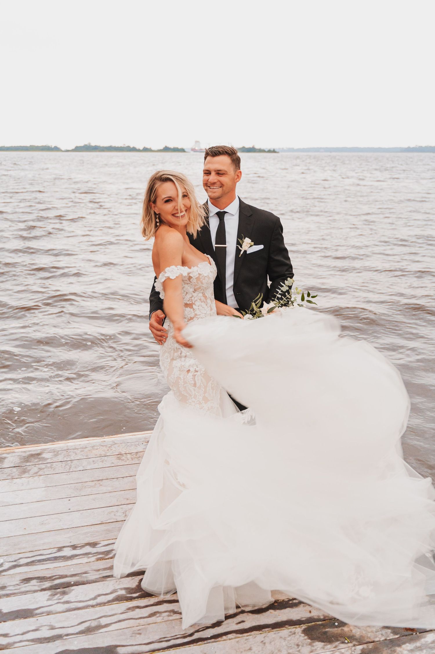 Bride and groom standing on a pier, smiling.