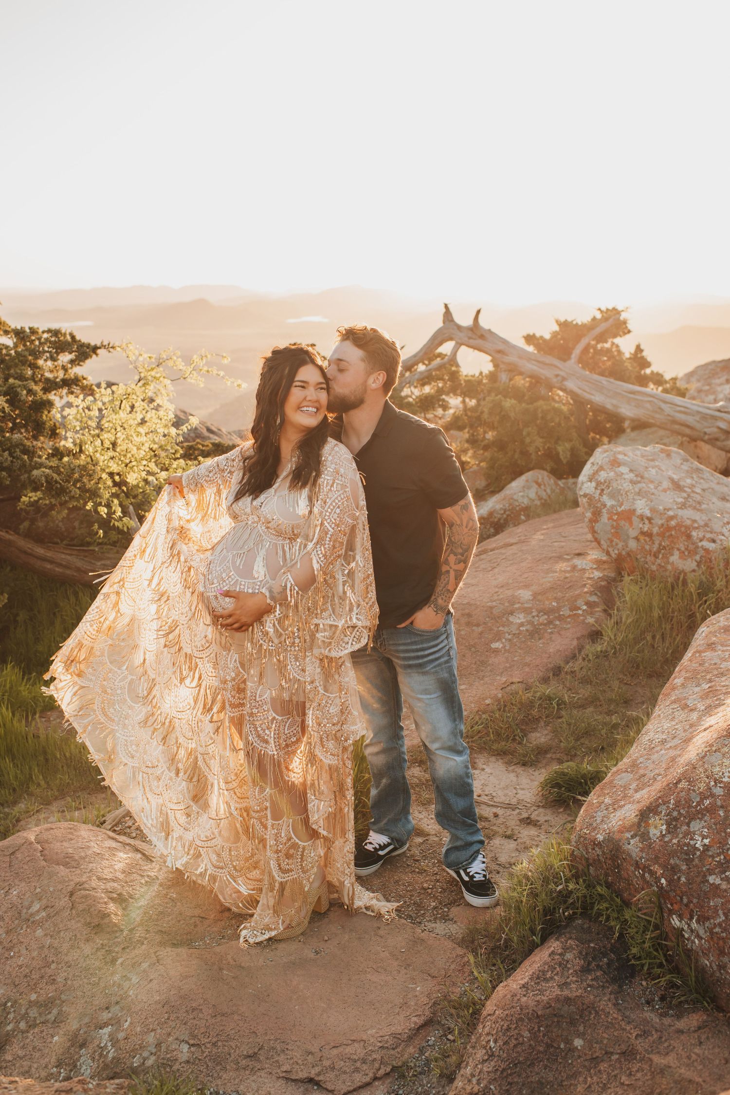 Pregnant woman and man standing in front of sunset covered rocks