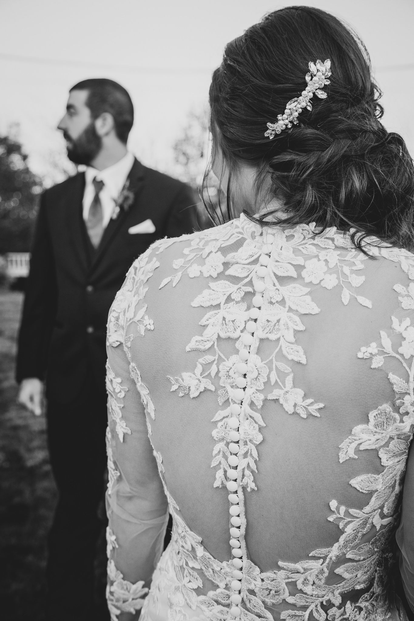 Black and white wedding photo showing intricate lace details on bride's dress back with floral hair accessory.