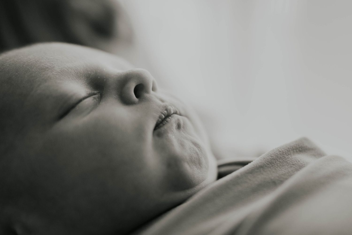 A sleeping baby rests peacefully in black and white tones against white bedding.