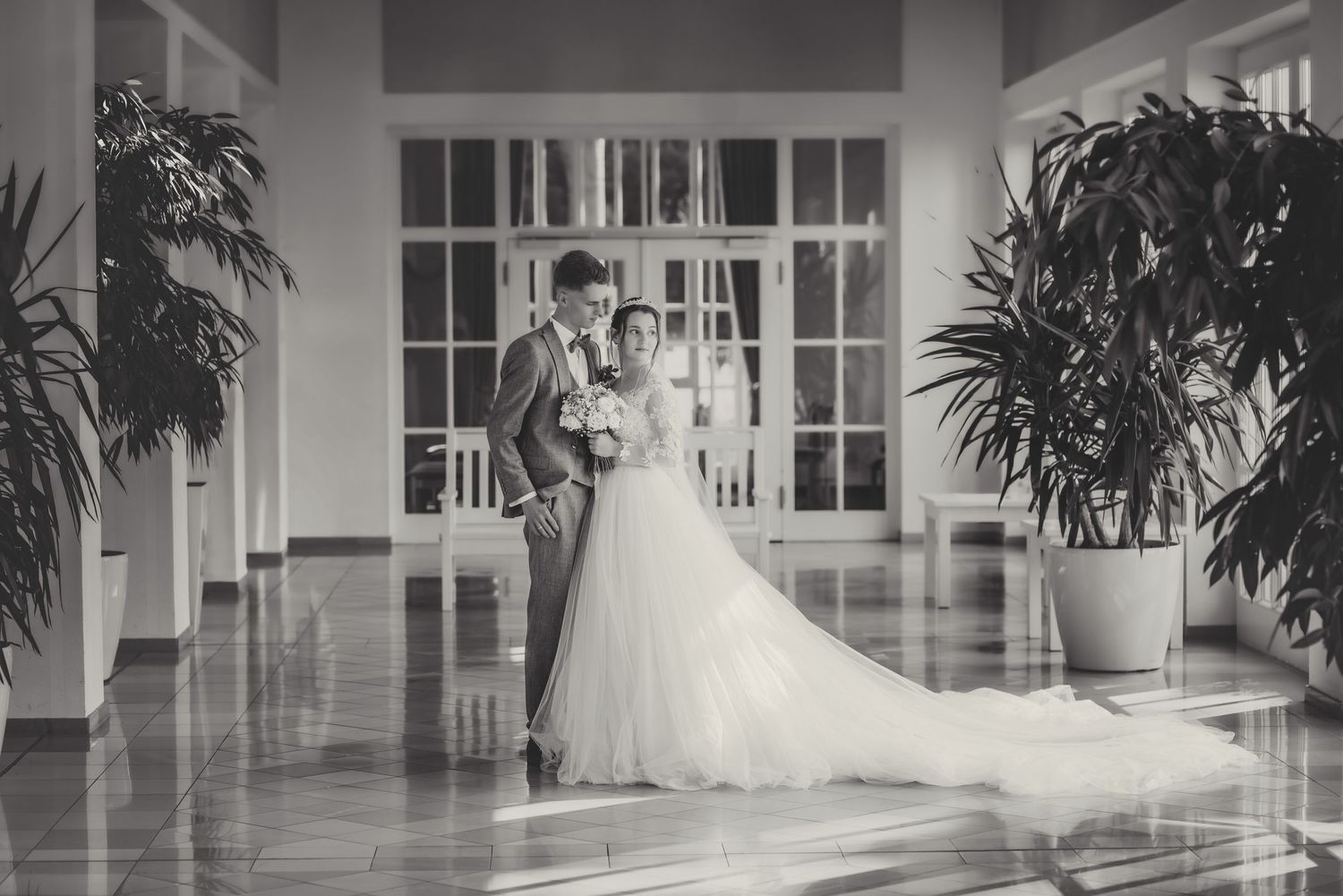 A black and white panoramic view of an elegant hallway with potted palm trees and arched doorways.