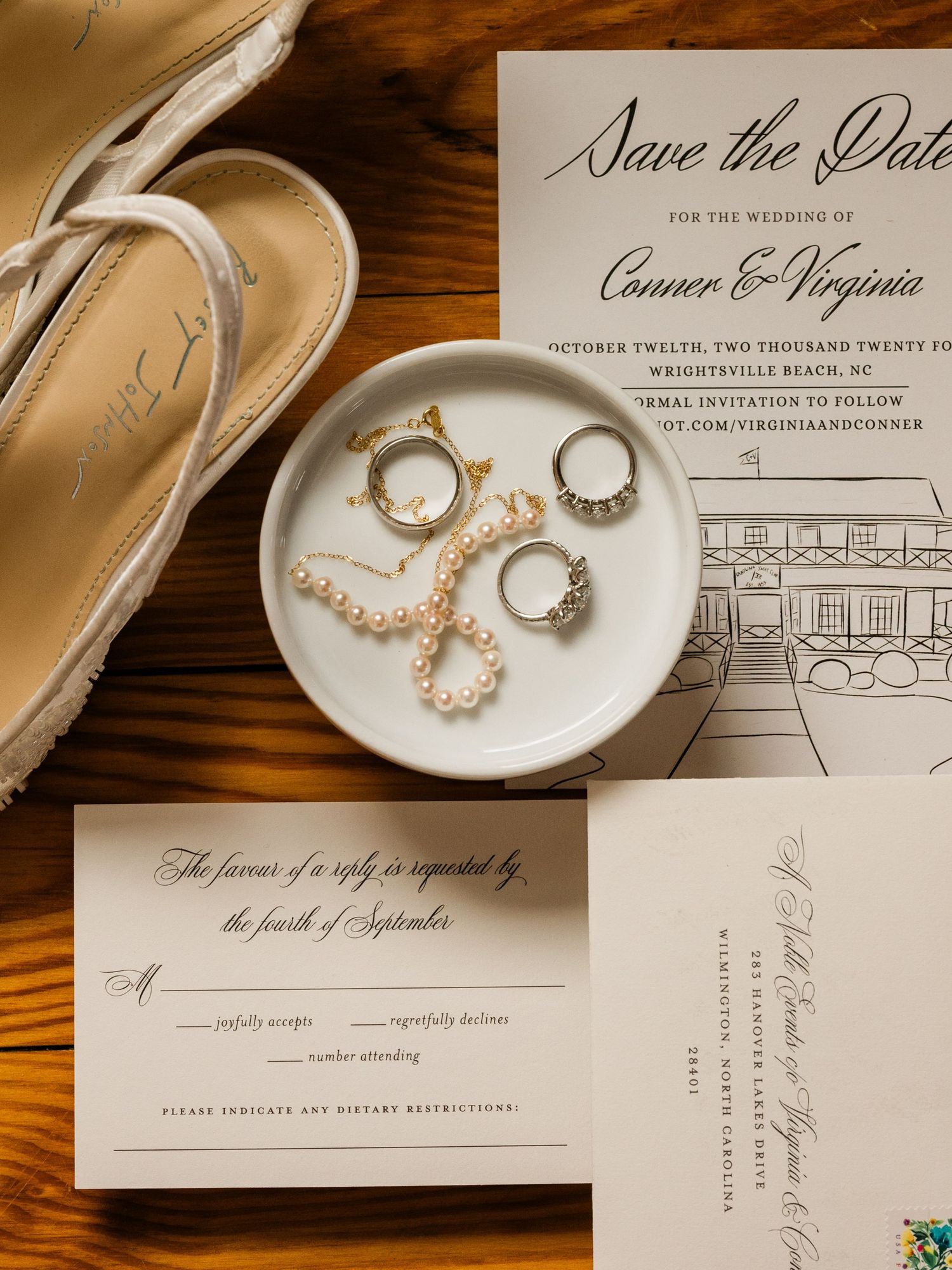 Wedding details flatlay with save the date invitation, rings, jewelry, and beige shoes on wooden surface.