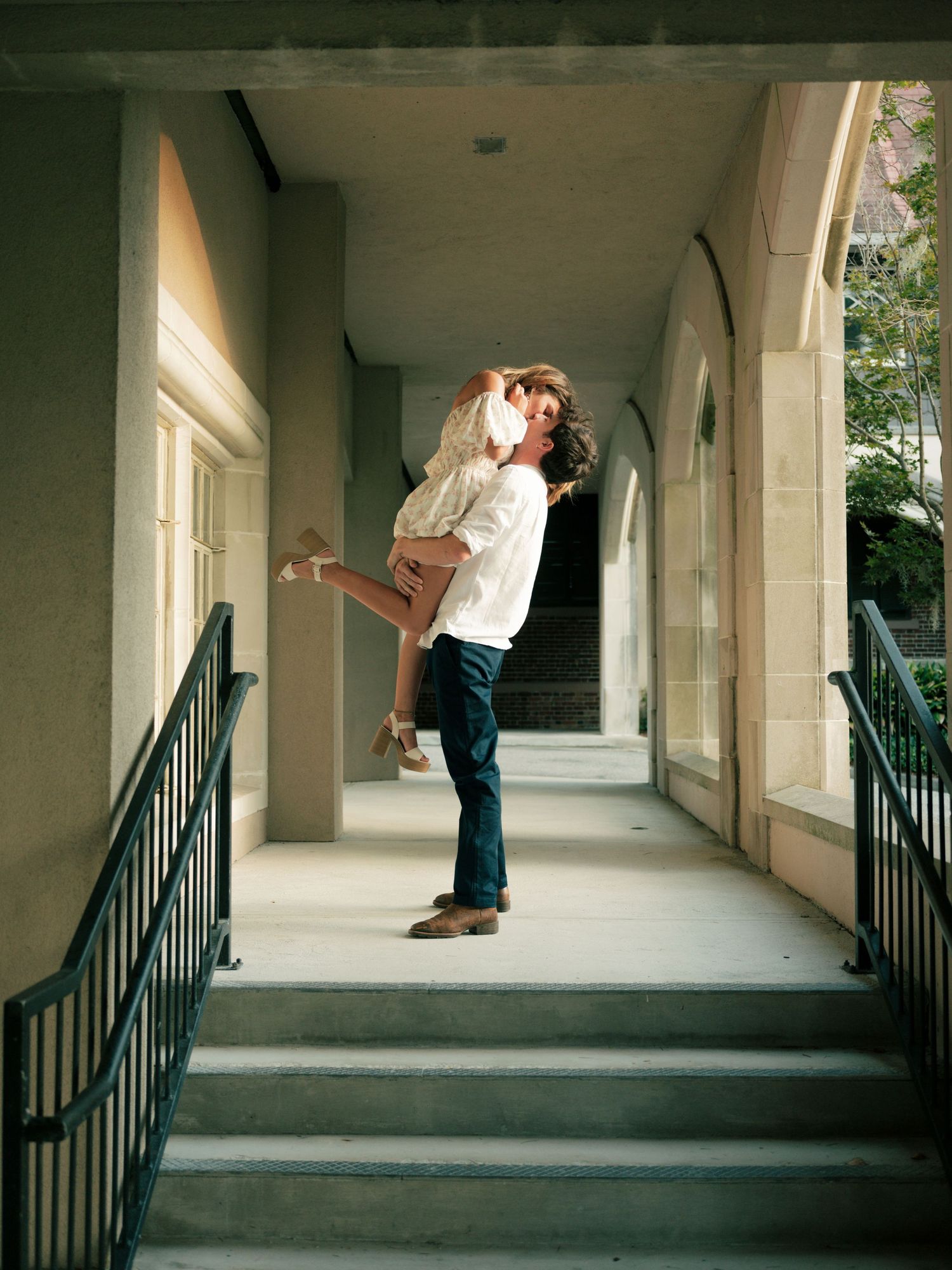 A joyful couple shares a tender moment in a covered walkway with arched columns and railings.