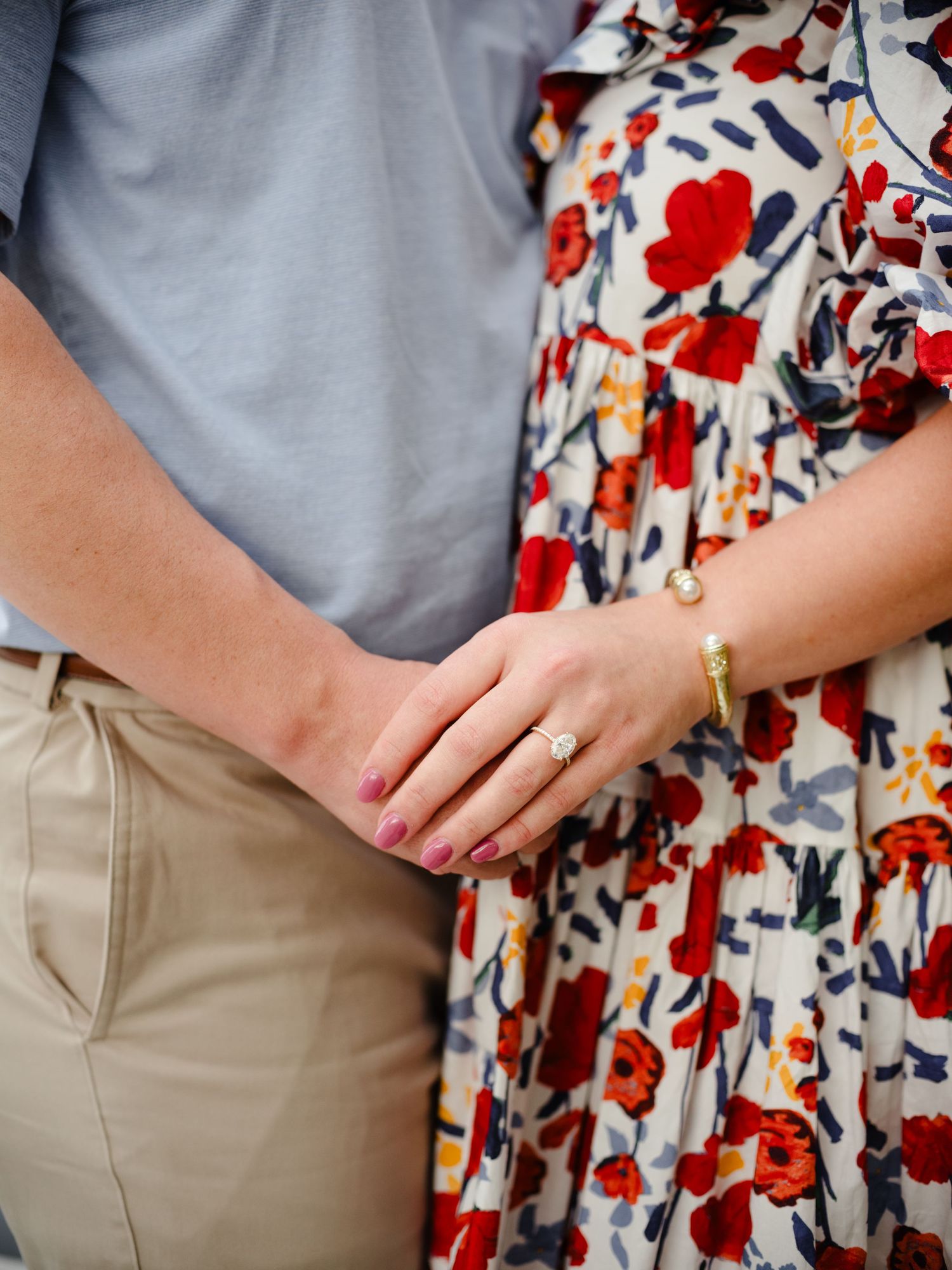 Close-up of hands showing engagement ring against floral dress and casual attire.