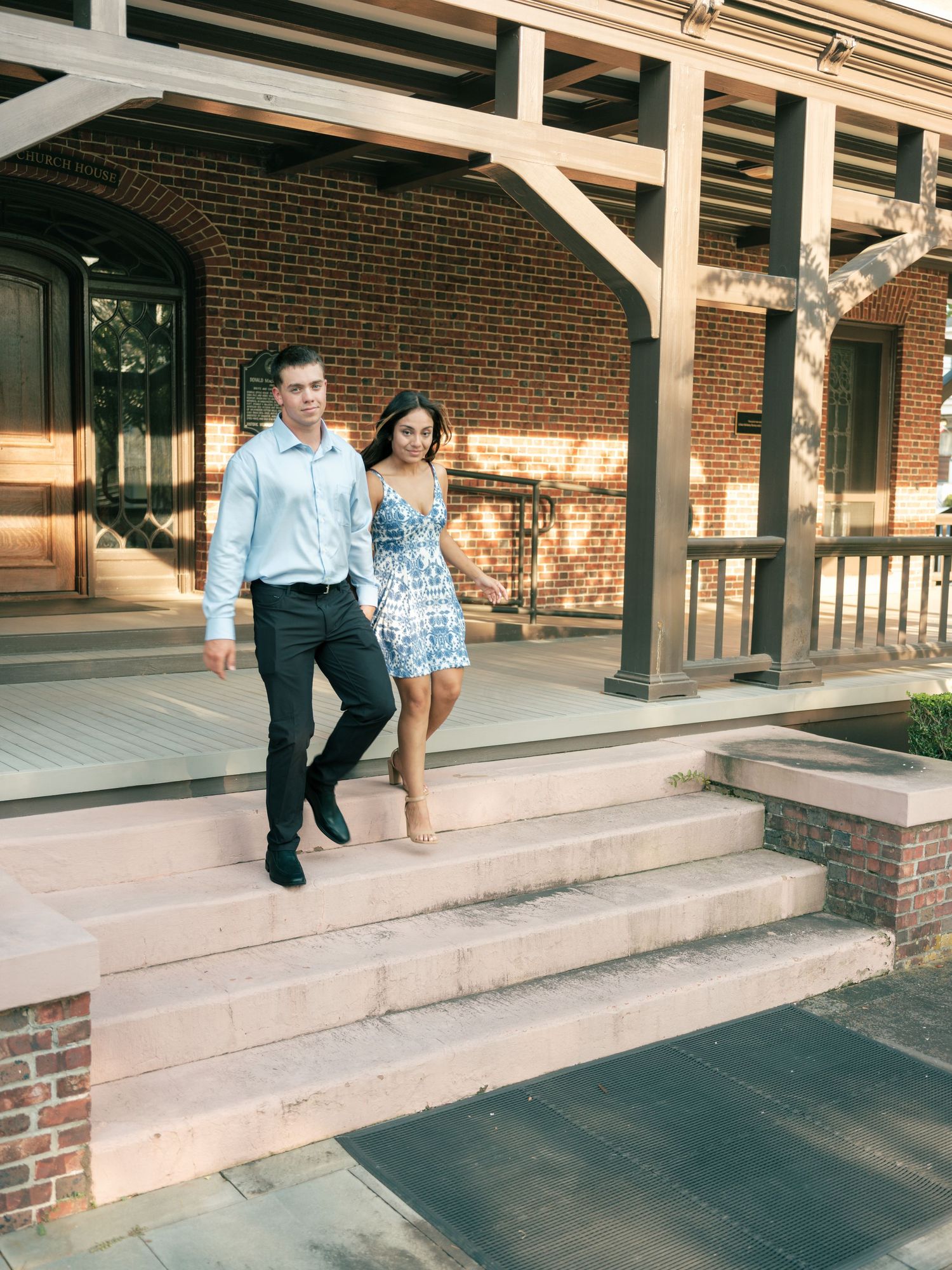 A couple descends stone steps at a historic brick building with white architectural beams and arched doorways.