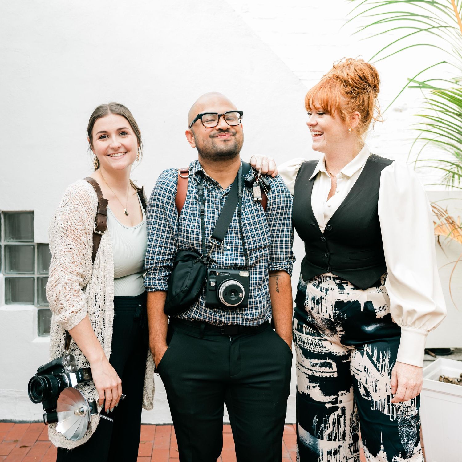Photography team poses with their gear against a white exterior wall.