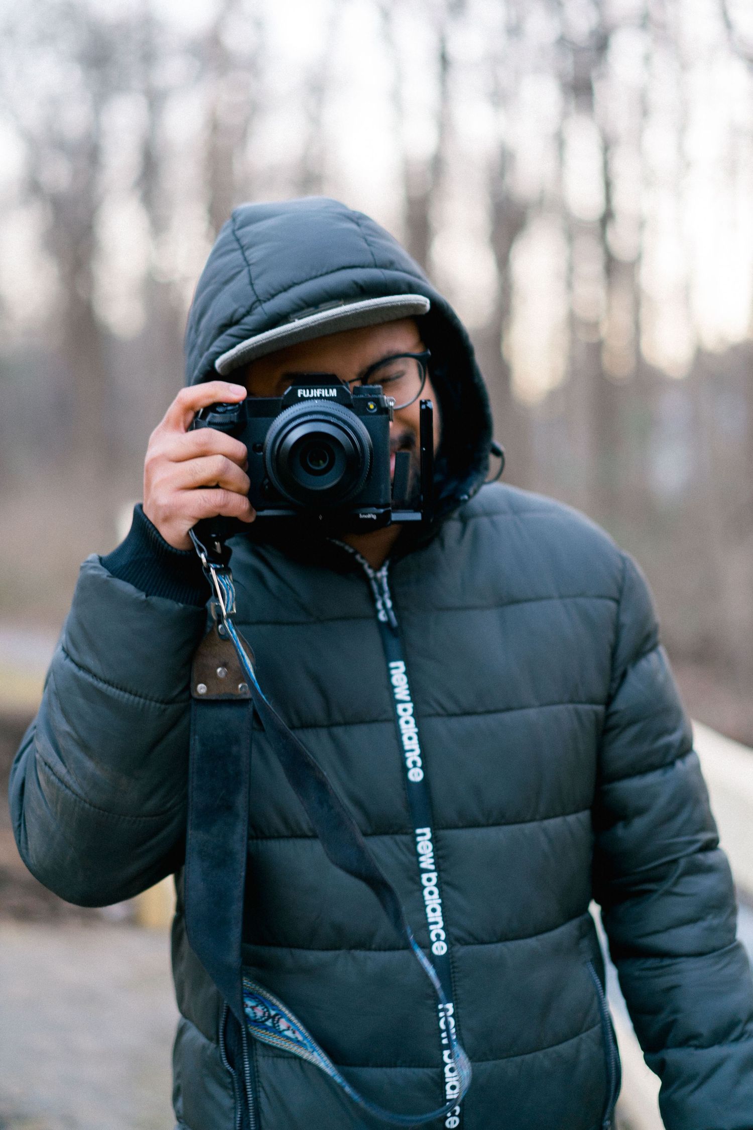 Winter photographer wearing puffy jacket and beanie takes photo with professional camera in woods.